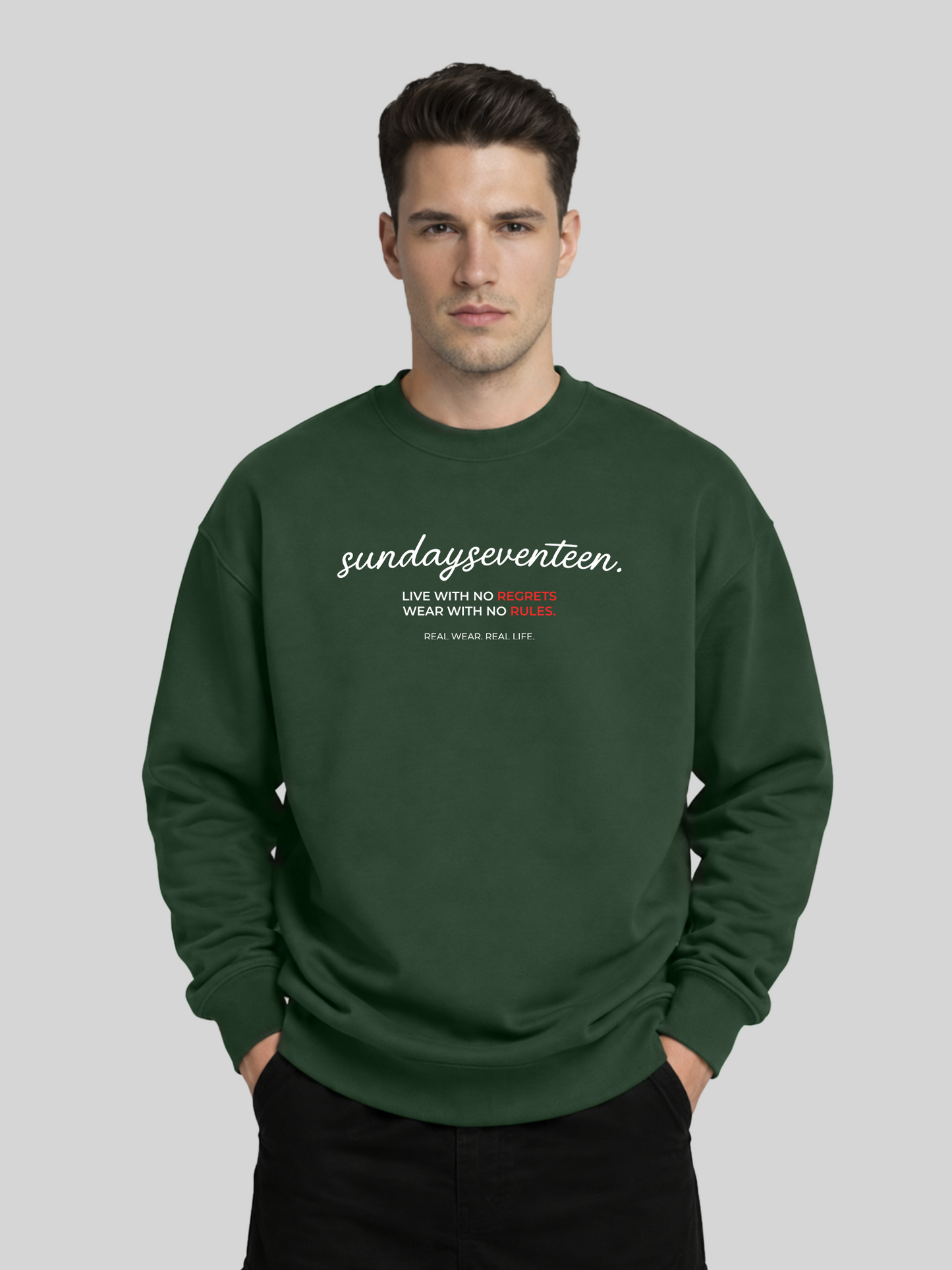 A front view of a male model wearing an olive green oversized crewneck sweatshirt with "sundayseventeen" printed in white script and red accents.