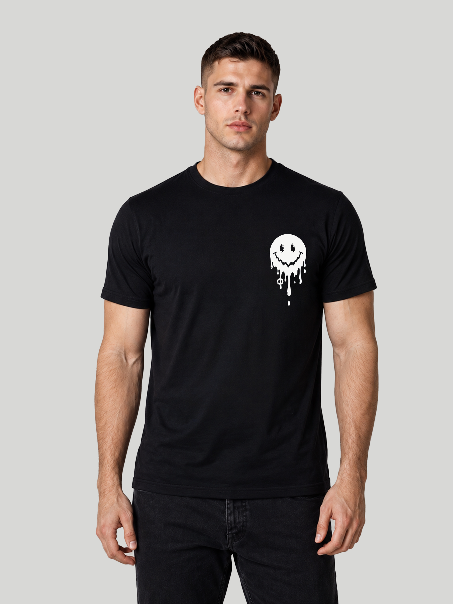 A front studio shot of a male model looking forward, wearing a black regular fit half-sleeve t-shirt with a small white melting smiley face graphic printed on the left chest.