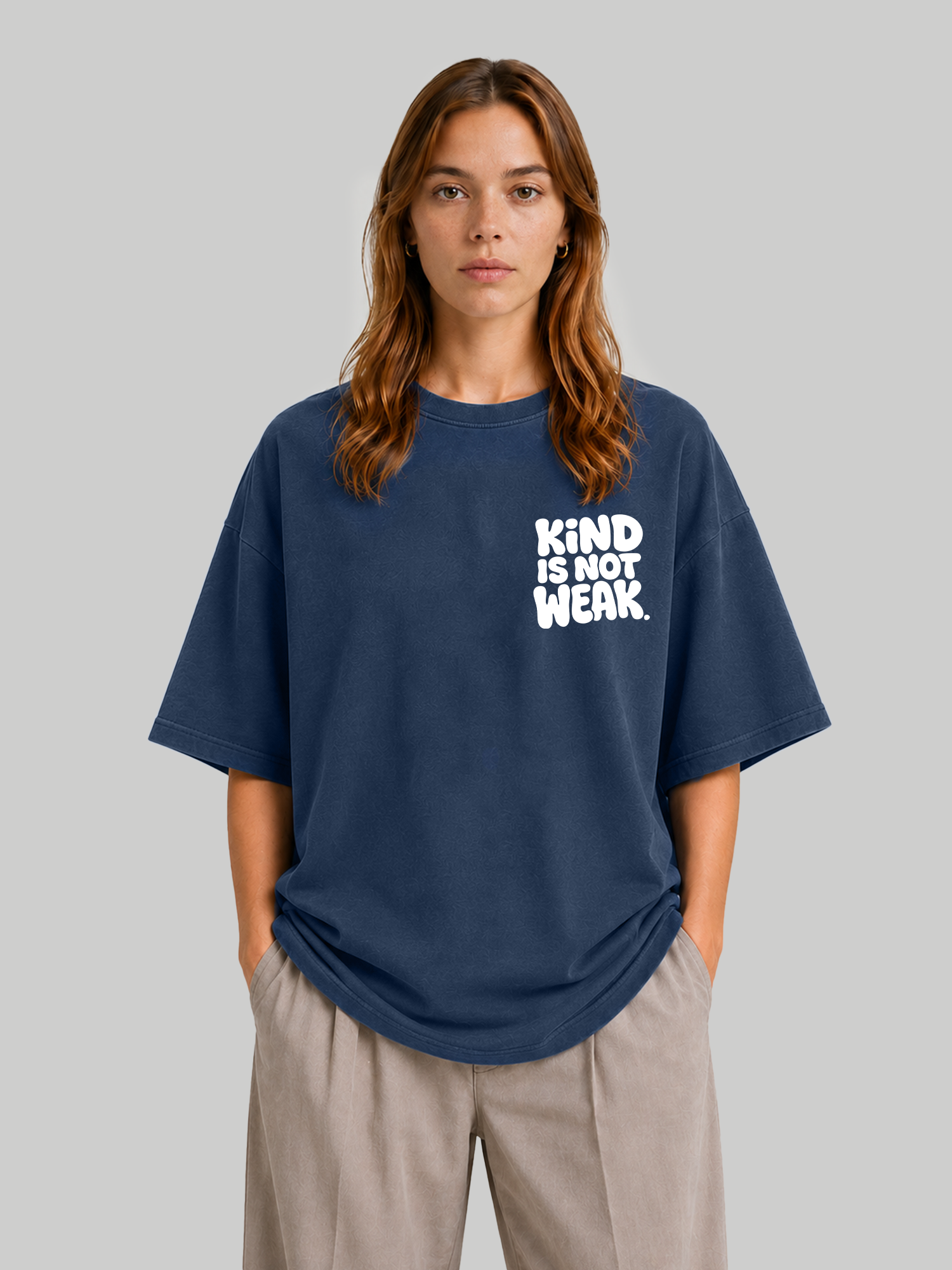 Women's oversized navy blue t-shirt with "Kind Is Not Weak" white chest print, hands in pockets.