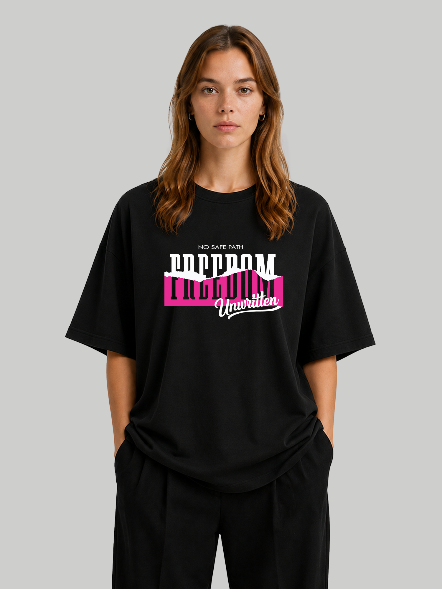 Women's oversized black statement t-shirt with "Freedom Unwritten" graphic print, relaxed front-facing pose with hands in pockets.