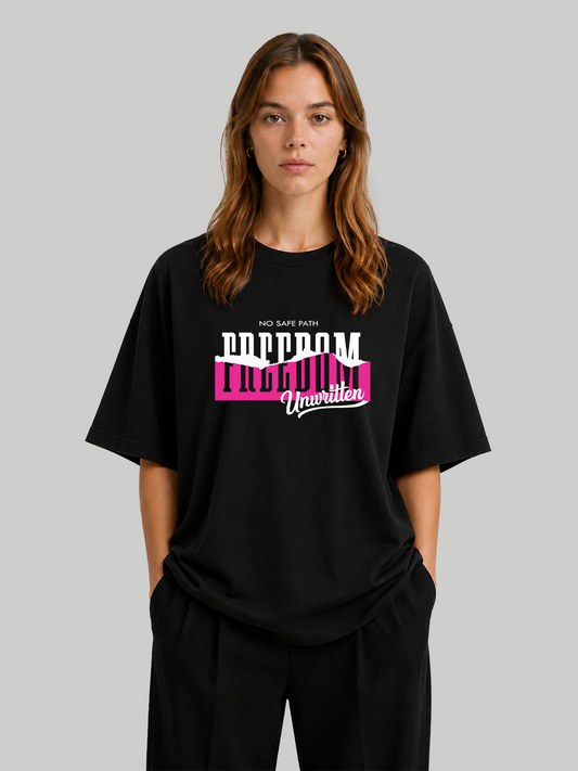 Women's oversized black statement t-shirt with "Freedom Unwritten" graphic print, relaxed front-facing pose with hands in pockets.