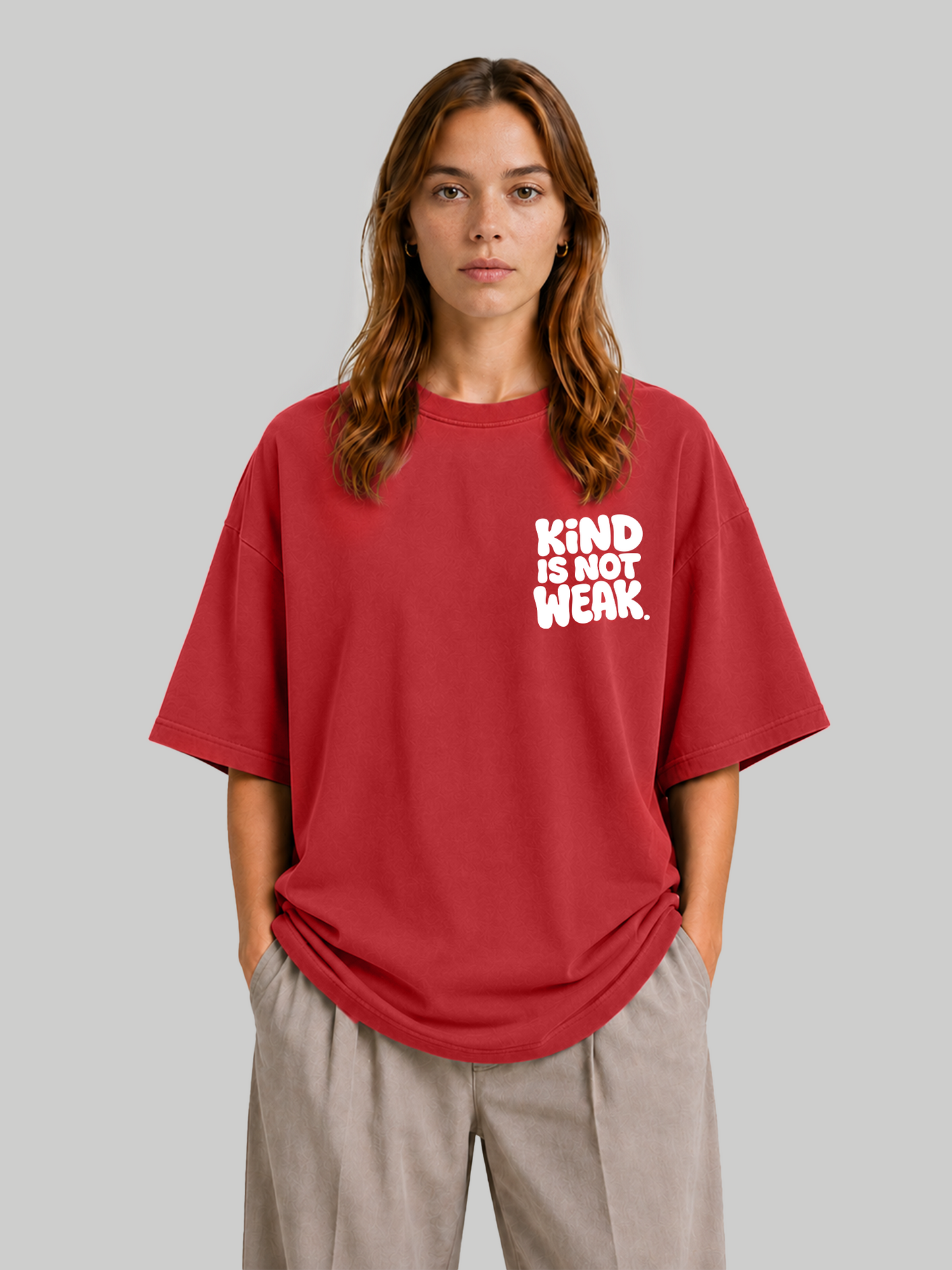 Women's oversized red graphic tee featuring "Kind Is Not Weak" design, front-facing view with hands in pockets.