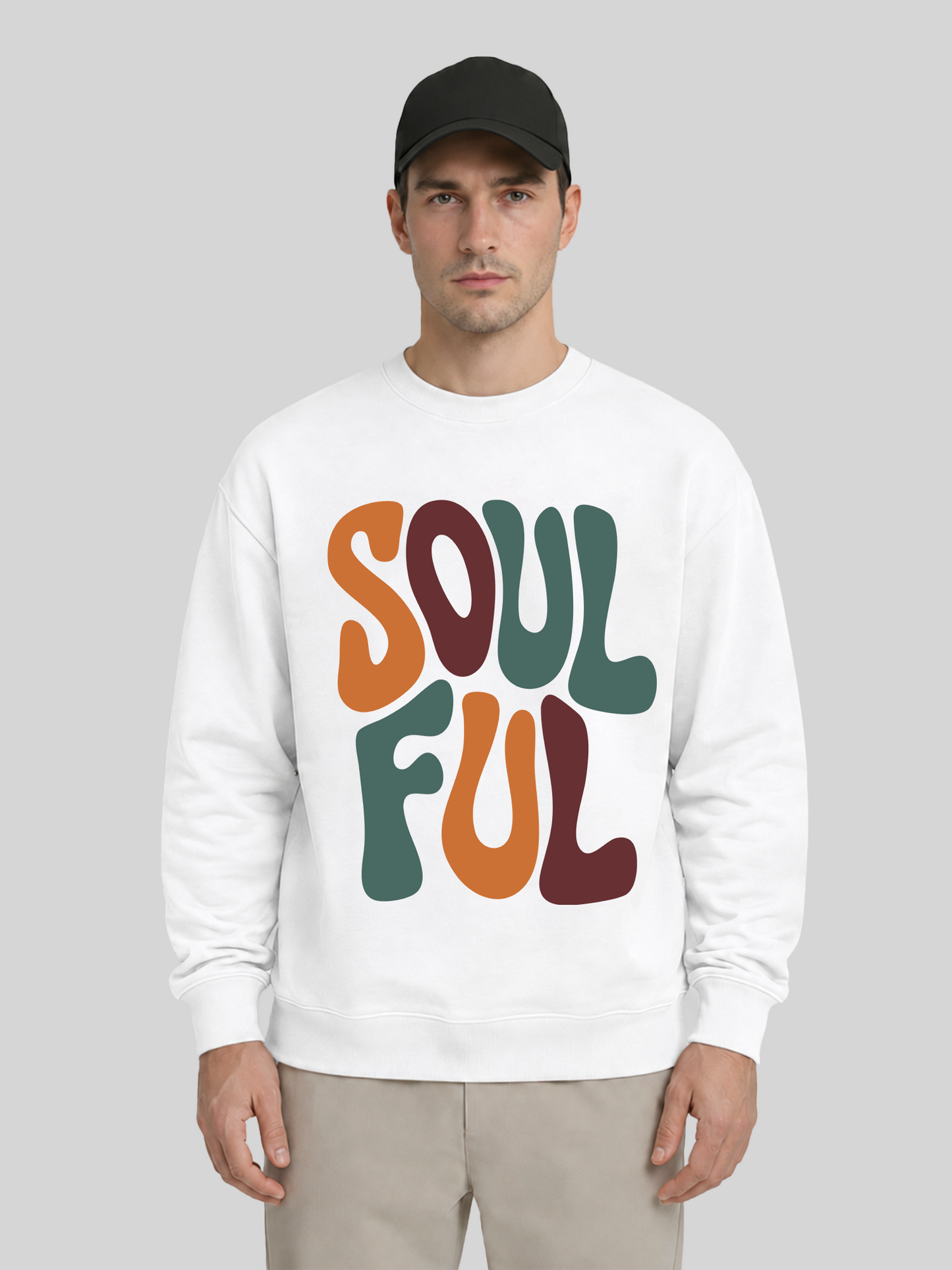 A full front view of a male model wearing a white premium sweatshirt with a large colorful "SOULFUL" graphic print, paired with a black cap and khaki trousers.