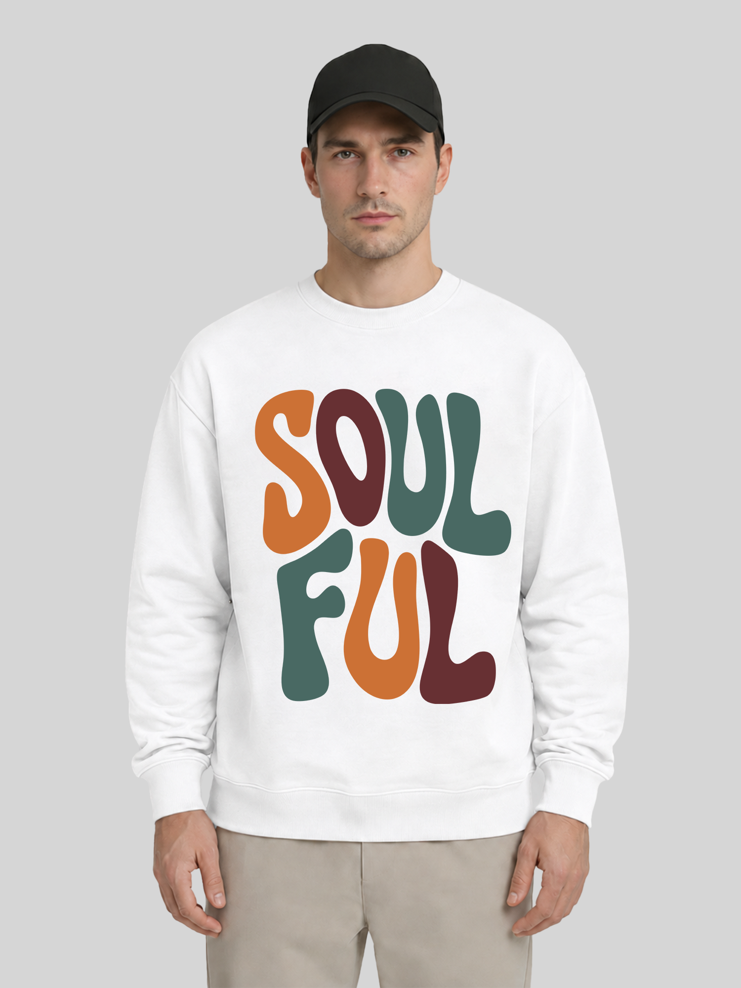 A full front view of a male model wearing a white premium sweatshirt with a large colorful "SOULFUL" graphic print, paired with a black cap and khaki trousers.