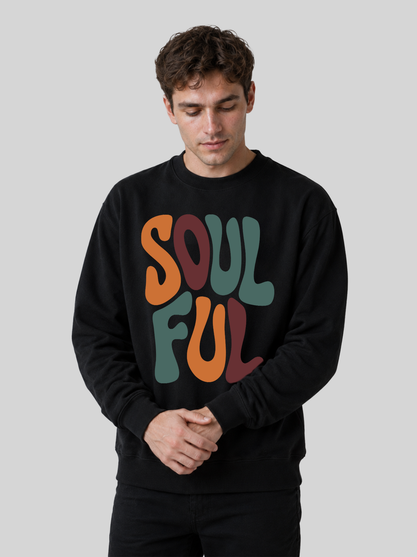 A male model looking down while clasping his hands together, wearing a black streetwear sweatshirt with a vibrant retro font pattern.