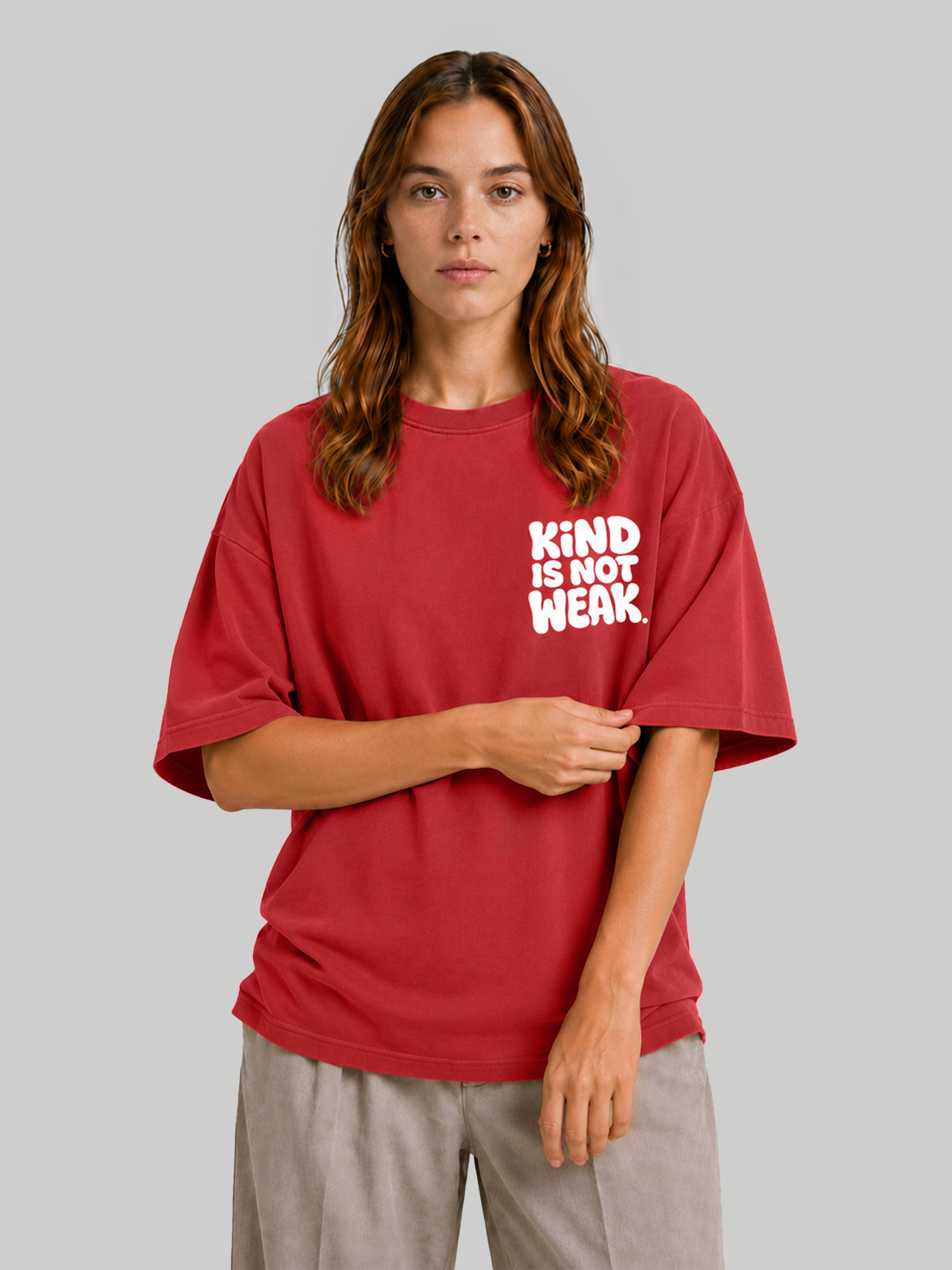Women's oversized red t-shirt with "Kind Is Not Weak" white chest print, model holding sleeve.