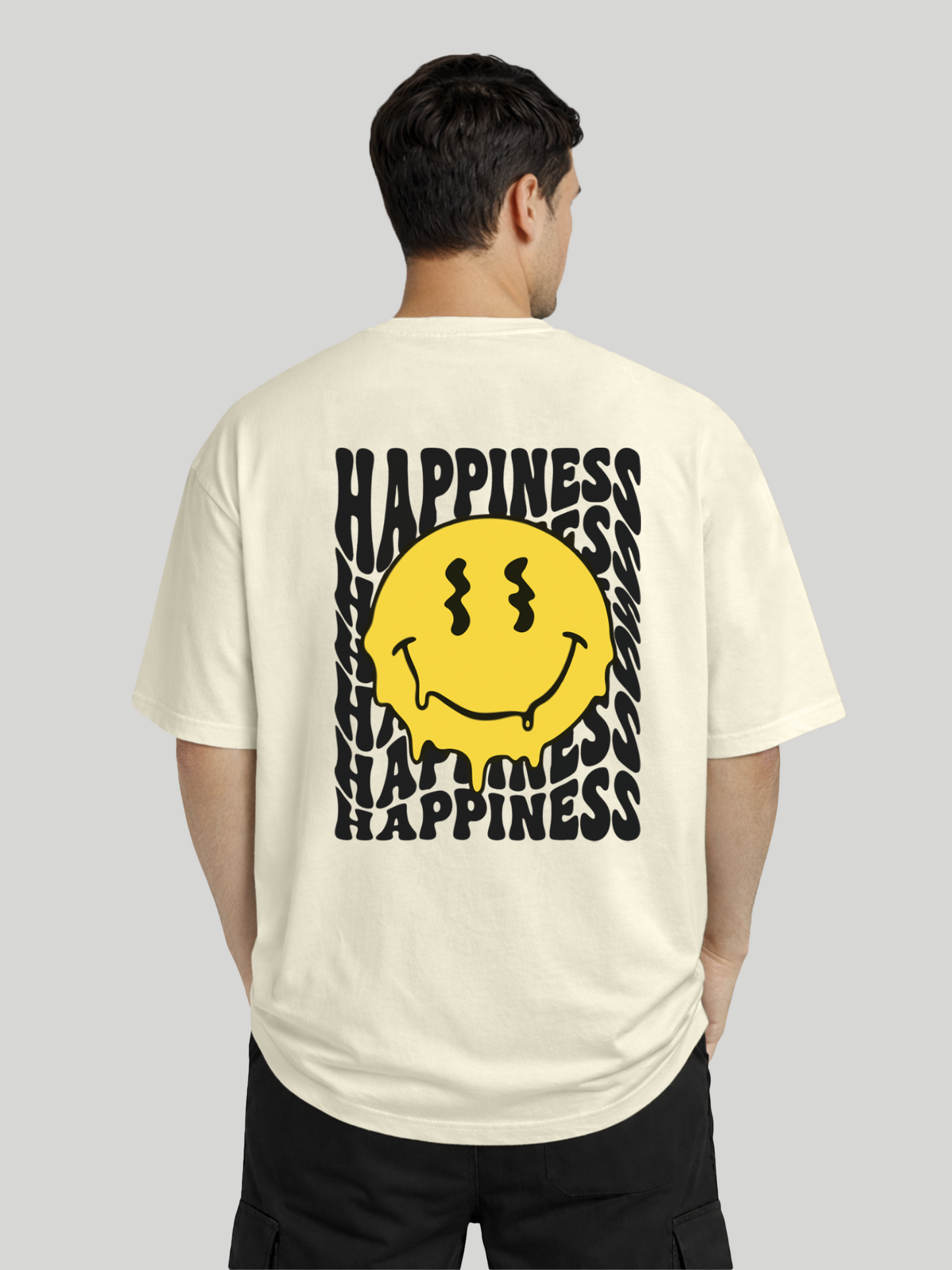 Back angled view of man wearing butter oversized t-shirt with Happiness back graphic and yellow dripping smiley print