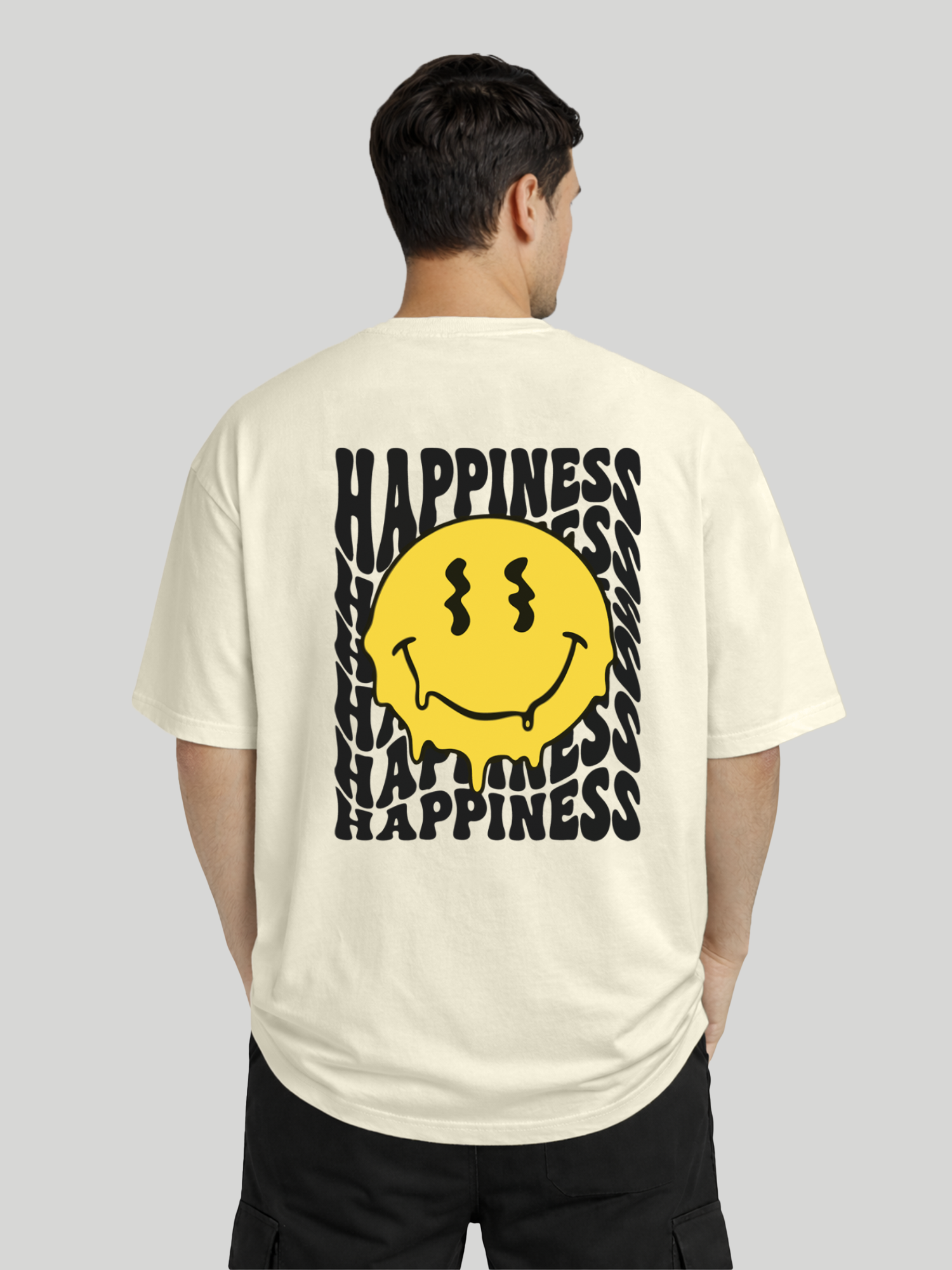 Back angled view of man wearing butter oversized t-shirt with Happiness back graphic and yellow dripping smiley print