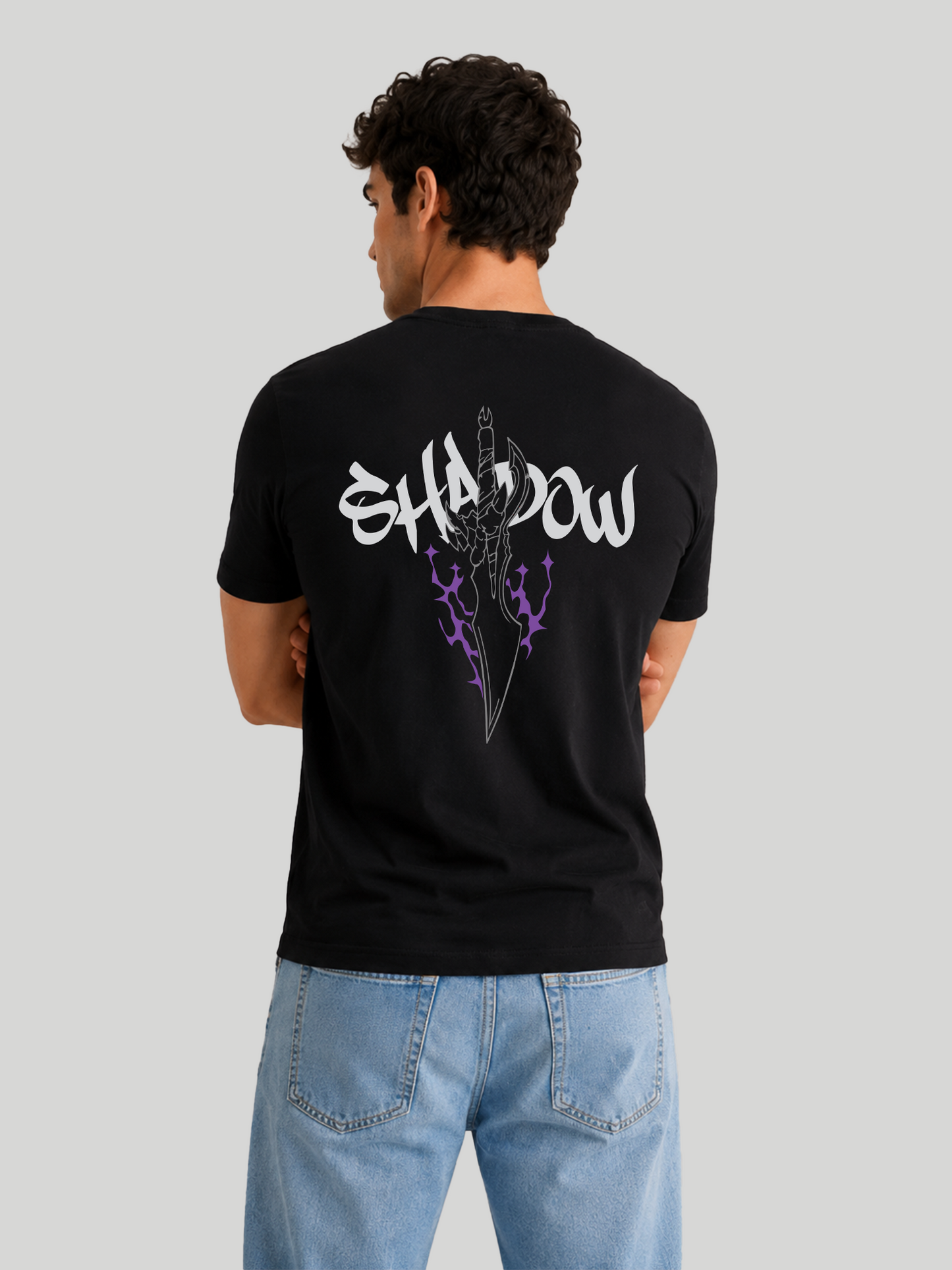 The back view of a male model standing with arms crossed, highlighting the shoulder drape and fabric structure of a black streetwear t-shirt with a dagger design.