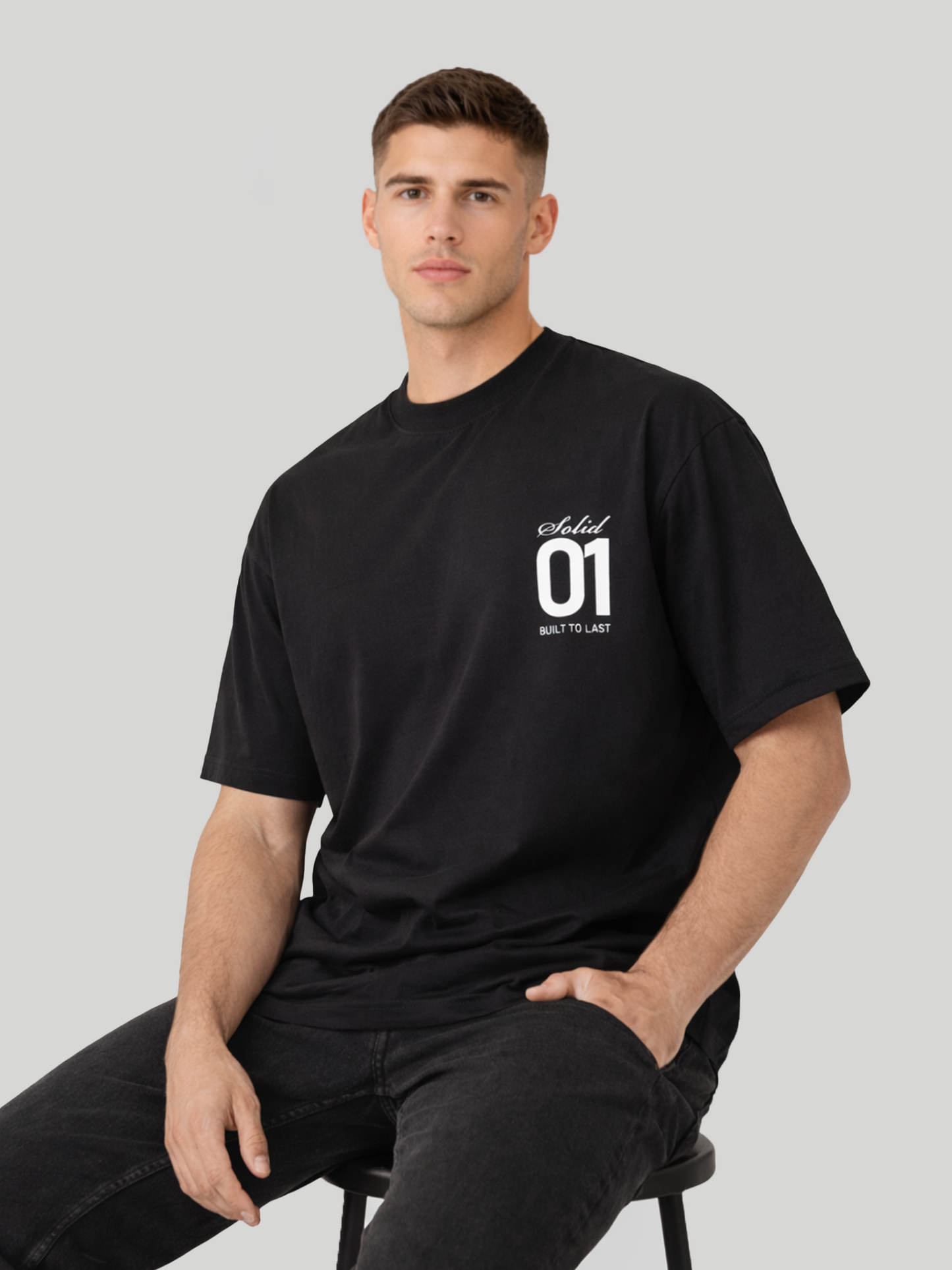 Man sitting on stool wearing black oversized t-shirt with Solid 01 chest print