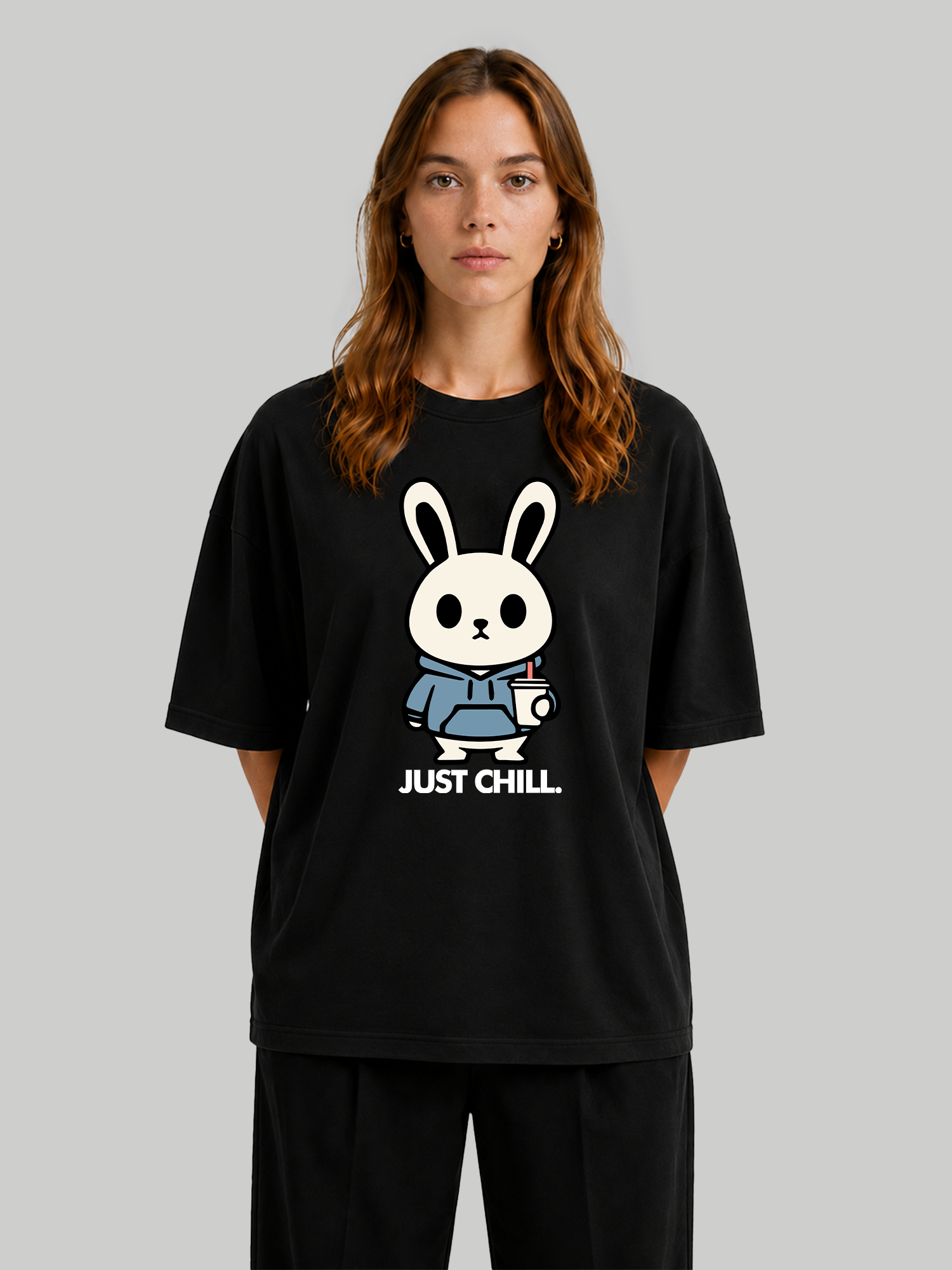 Women's oversized black graphic t-shirt featuring a cute bunny character in a blue hoodie with "Just Chill" text, front view with hands behind back.