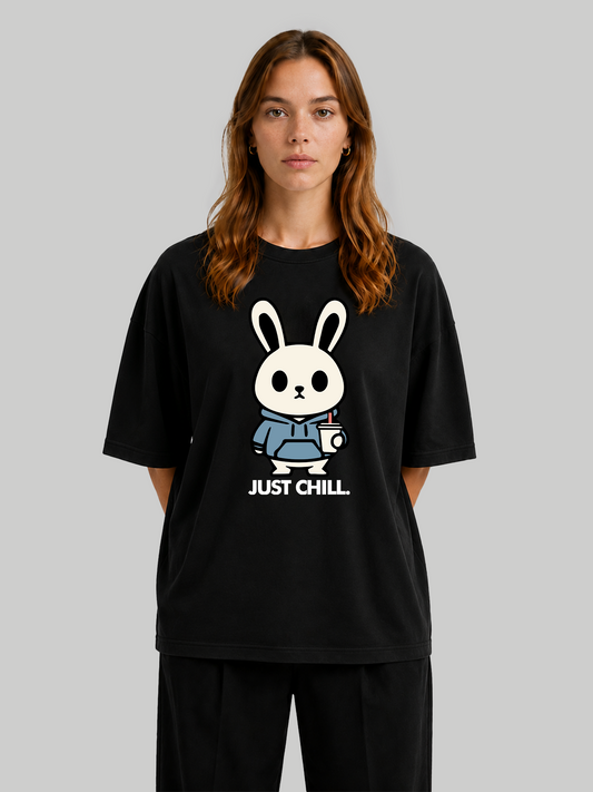 Women's oversized black graphic t-shirt featuring a cute bunny character in a blue hoodie with "Just Chill" text, front view with hands behind back.