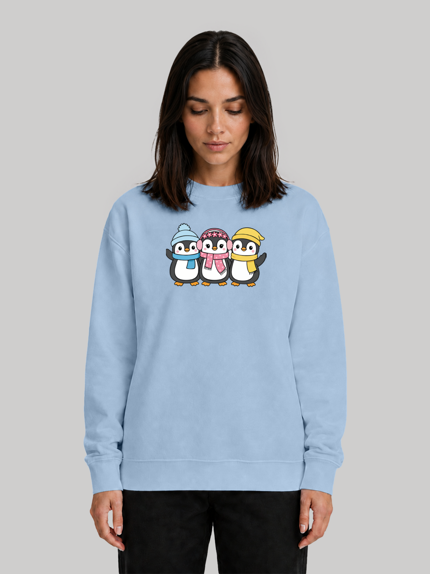 A female model looking down slightly, showcasing a baby blue long-sleeve crewneck sweatshirt with a playful cartoon penguin graphic.