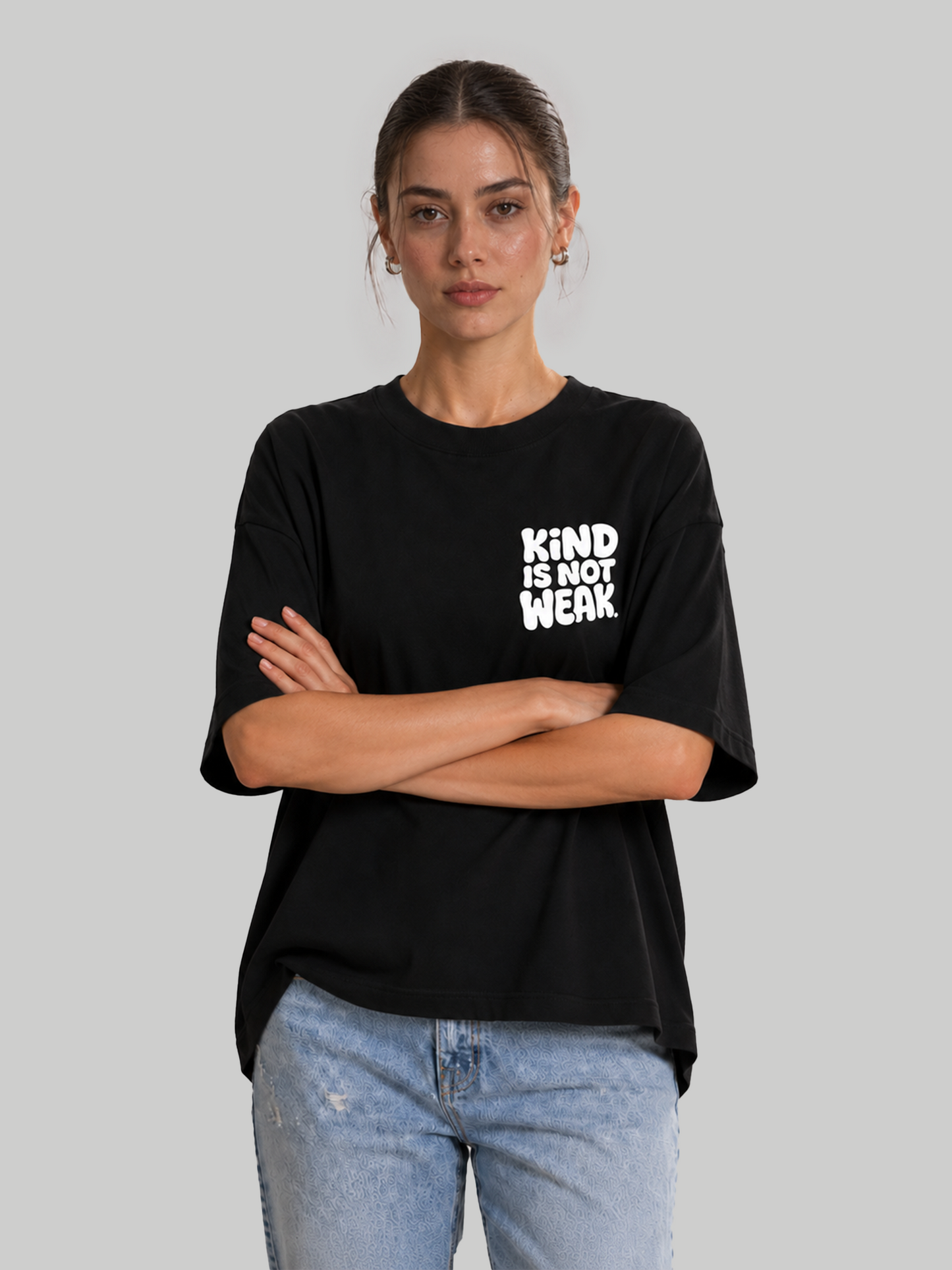 Women's oversized black graphic t-shirt with "Kind Is Not Weak" print, model standing with arms crossed.