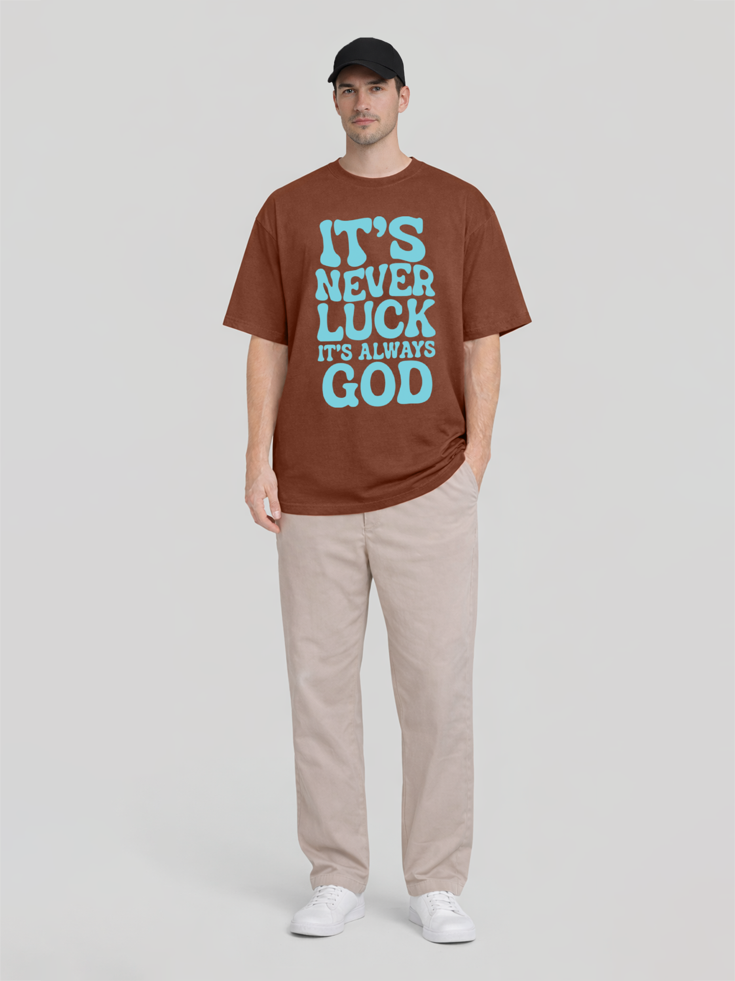 Full body front view of man wearing clay oversized graphic t-shirt with It’s Never Luck It’s Always God front print and black cap
