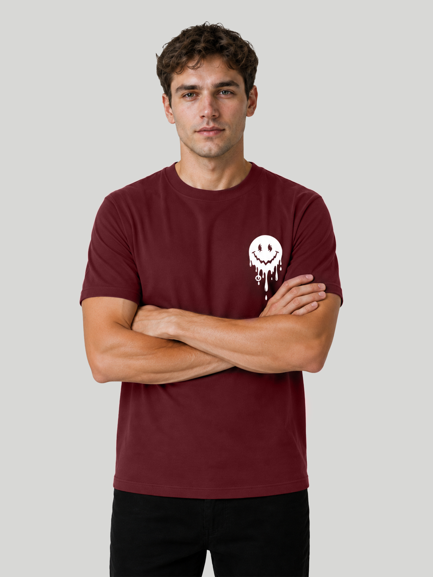 A front view of a male model standing with his arms crossed, wearing a maroon crewneck half-sleeve t-shirt with a small white melting smiley face graphic printed on the left chest.