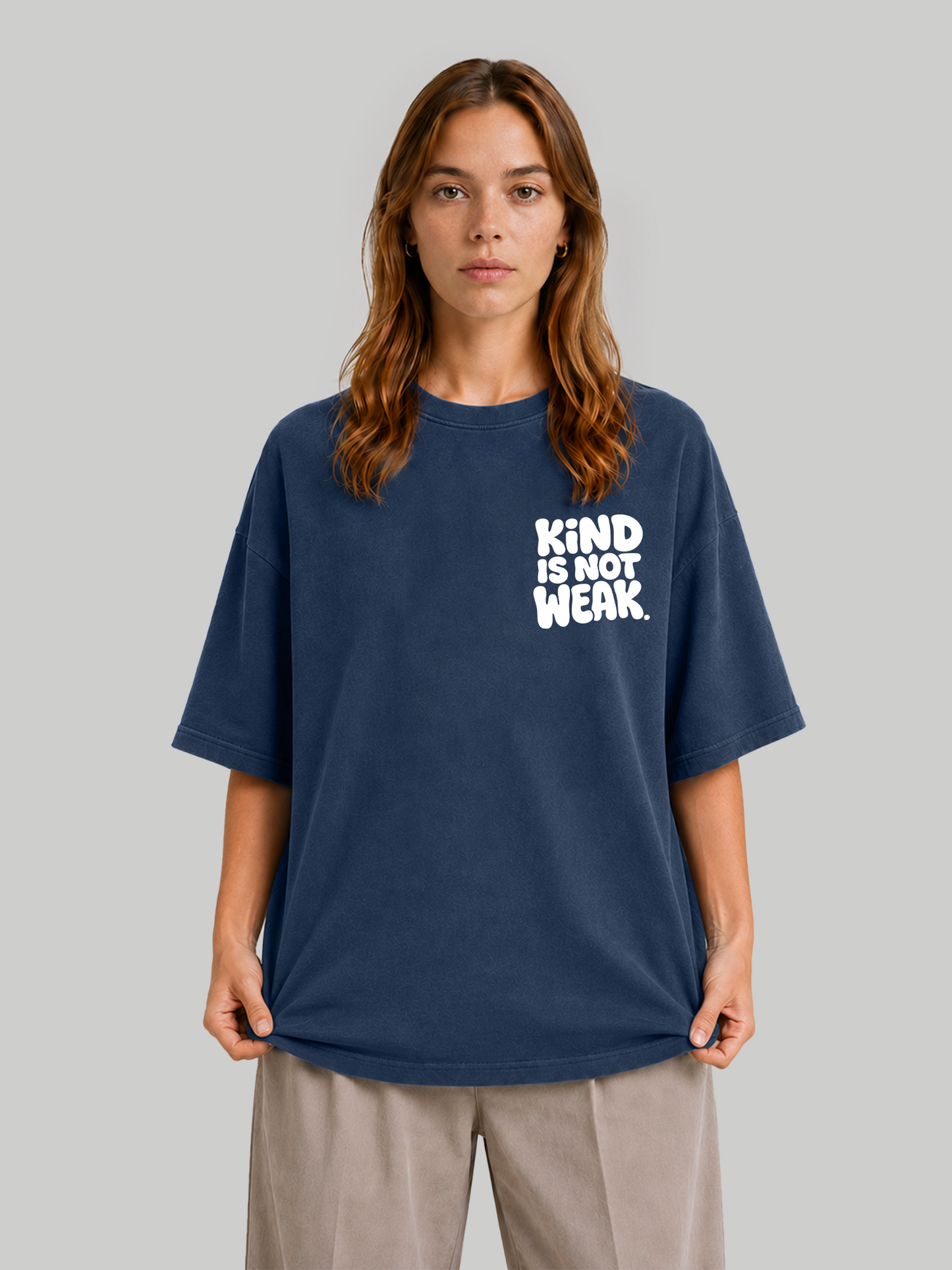 Women's oversized navy blue graphic tee featuring "Kind Is Not Weak" design, model holding sleeves.