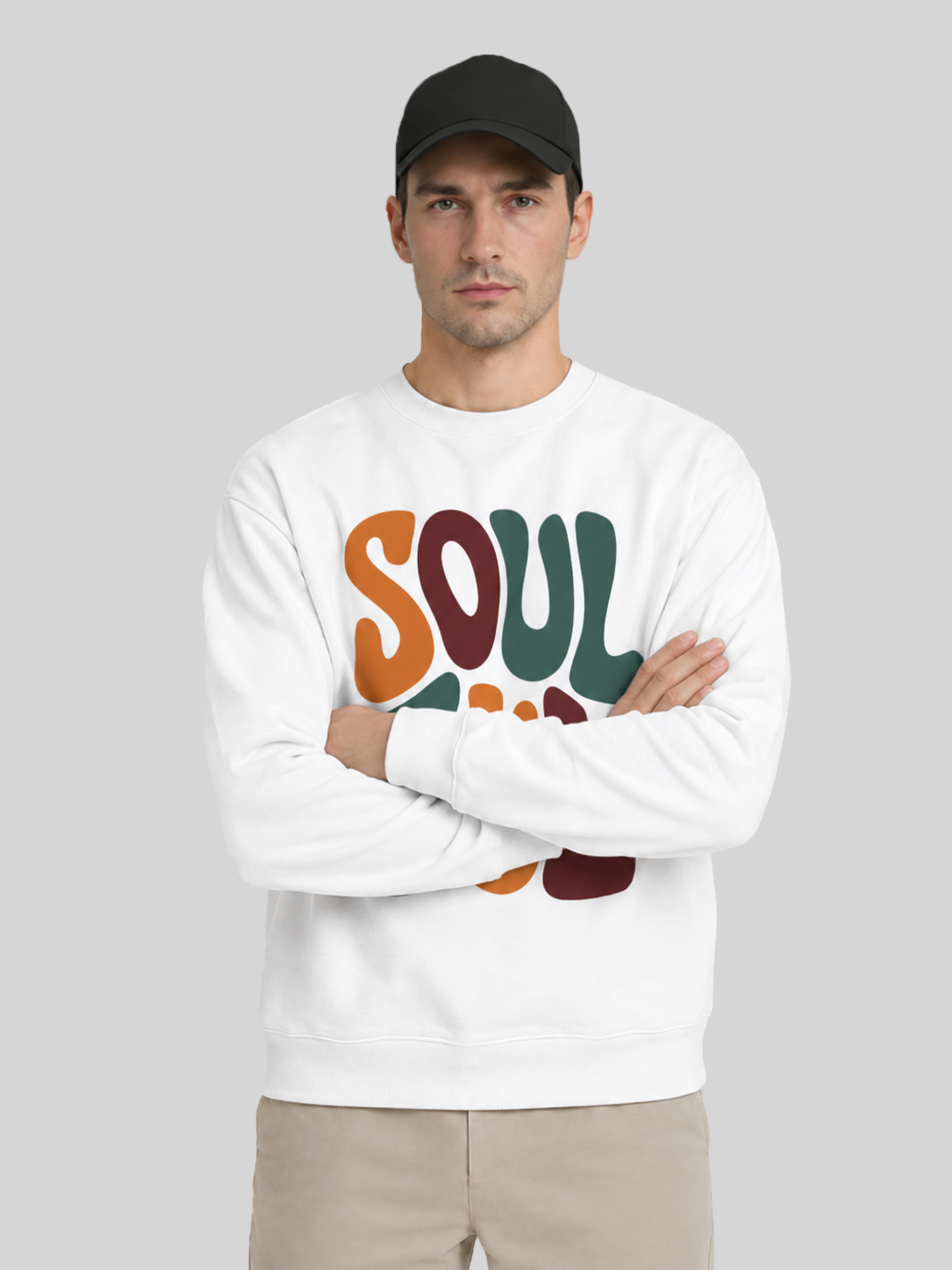 A male model wearing a black cap and a white custom printed sweatshirt while sitting on a stool, showcasing a comfortable casual look.