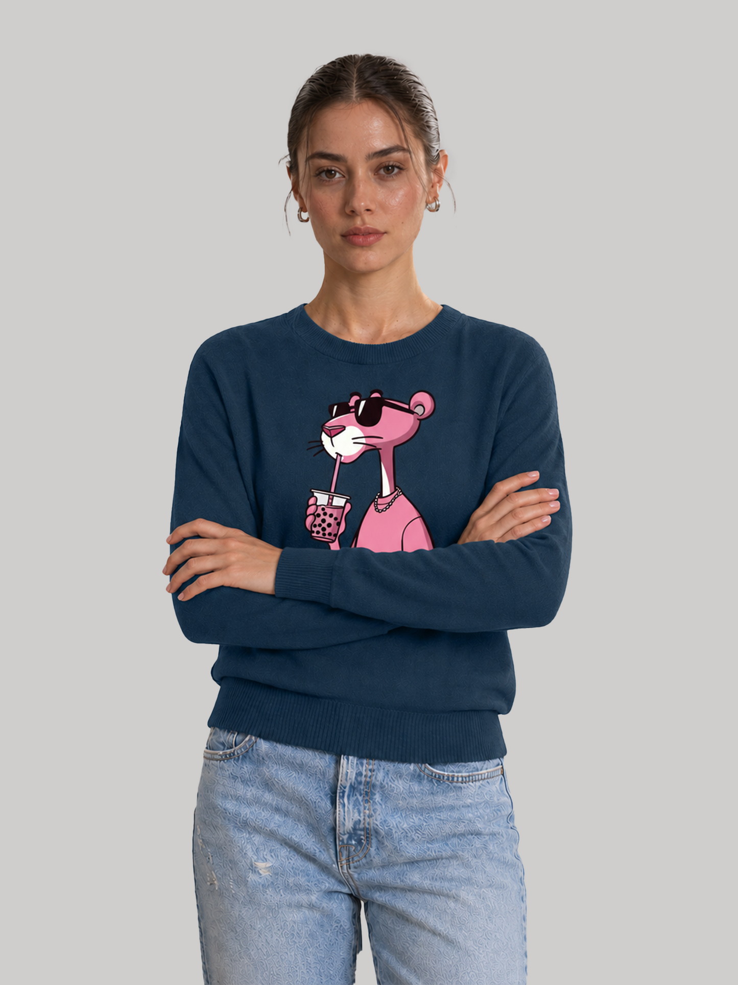 A front studio shot of a female model standing with her arms crossed, wearing a casual navy blue sweatshirt with a custom pink character illustration.