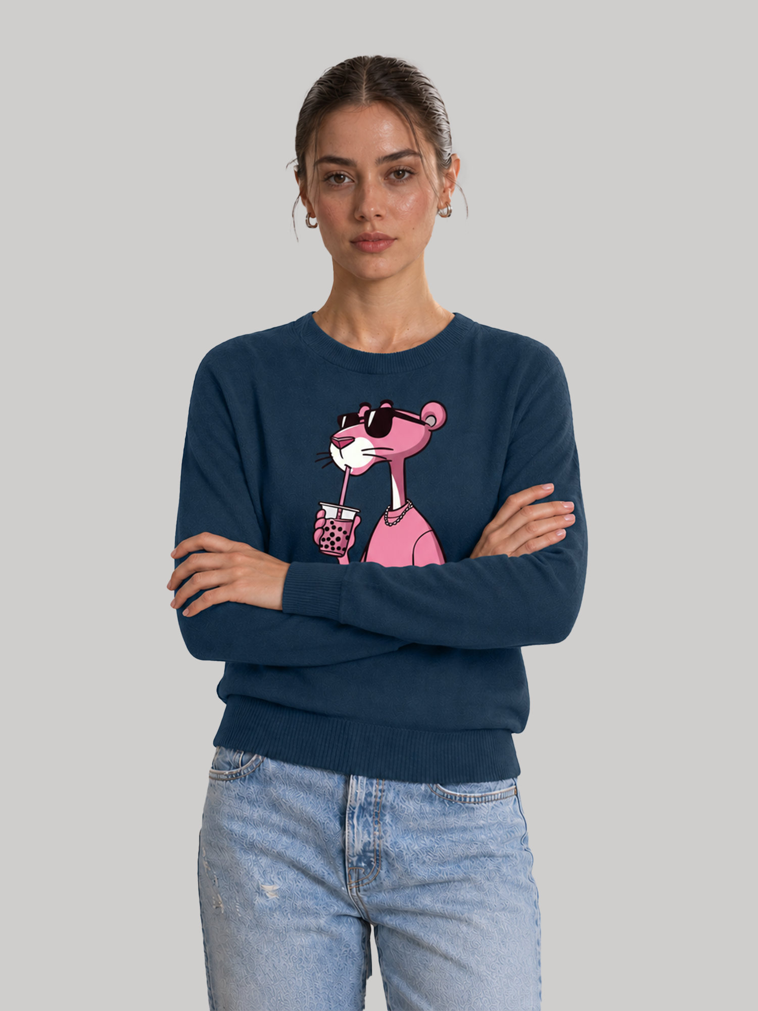 A front studio shot of a female model standing with her arms crossed, wearing a casual navy blue sweatshirt with a custom pink character illustration.