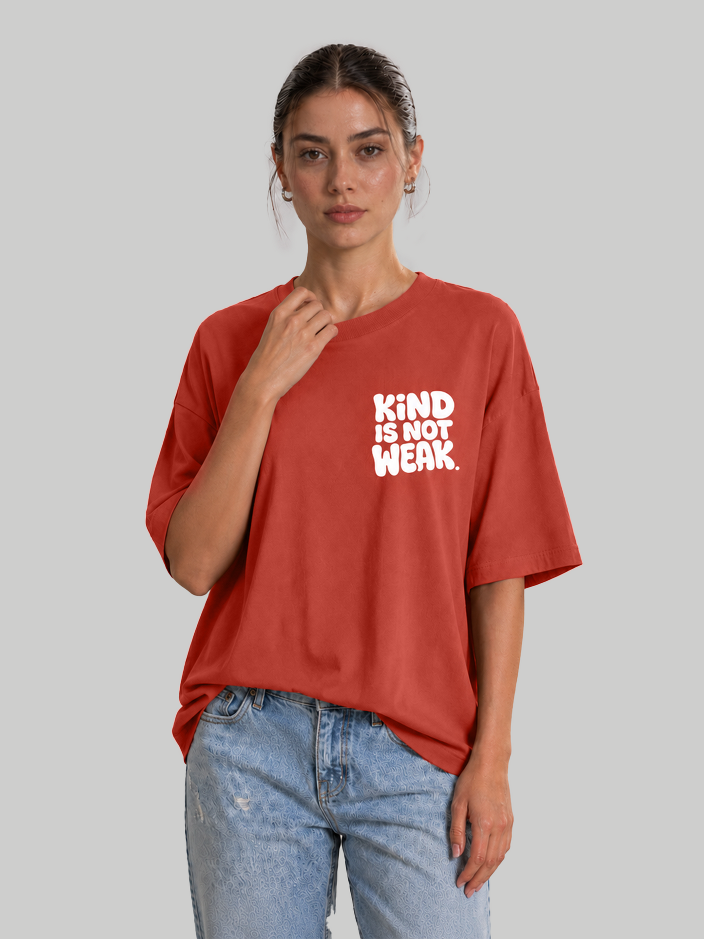 Women's oversized brick red graphic tee featuring "Kind Is Not Weak" design, model touching collar.
