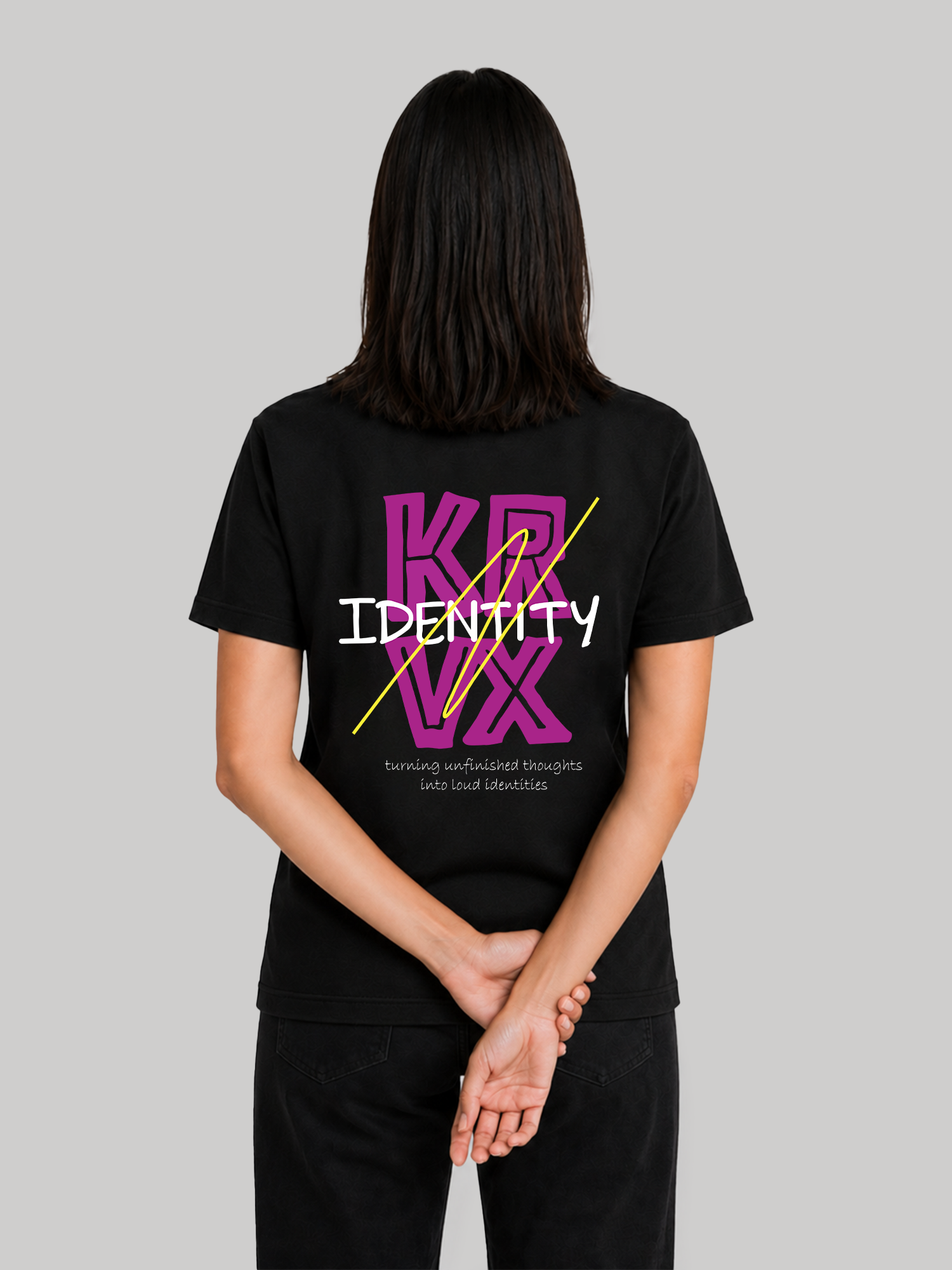 A straight rear view of a female model standing with her hands clasped behind her back, showcasing the regular fit of a black custom printed graphic streetwear t-shirt.