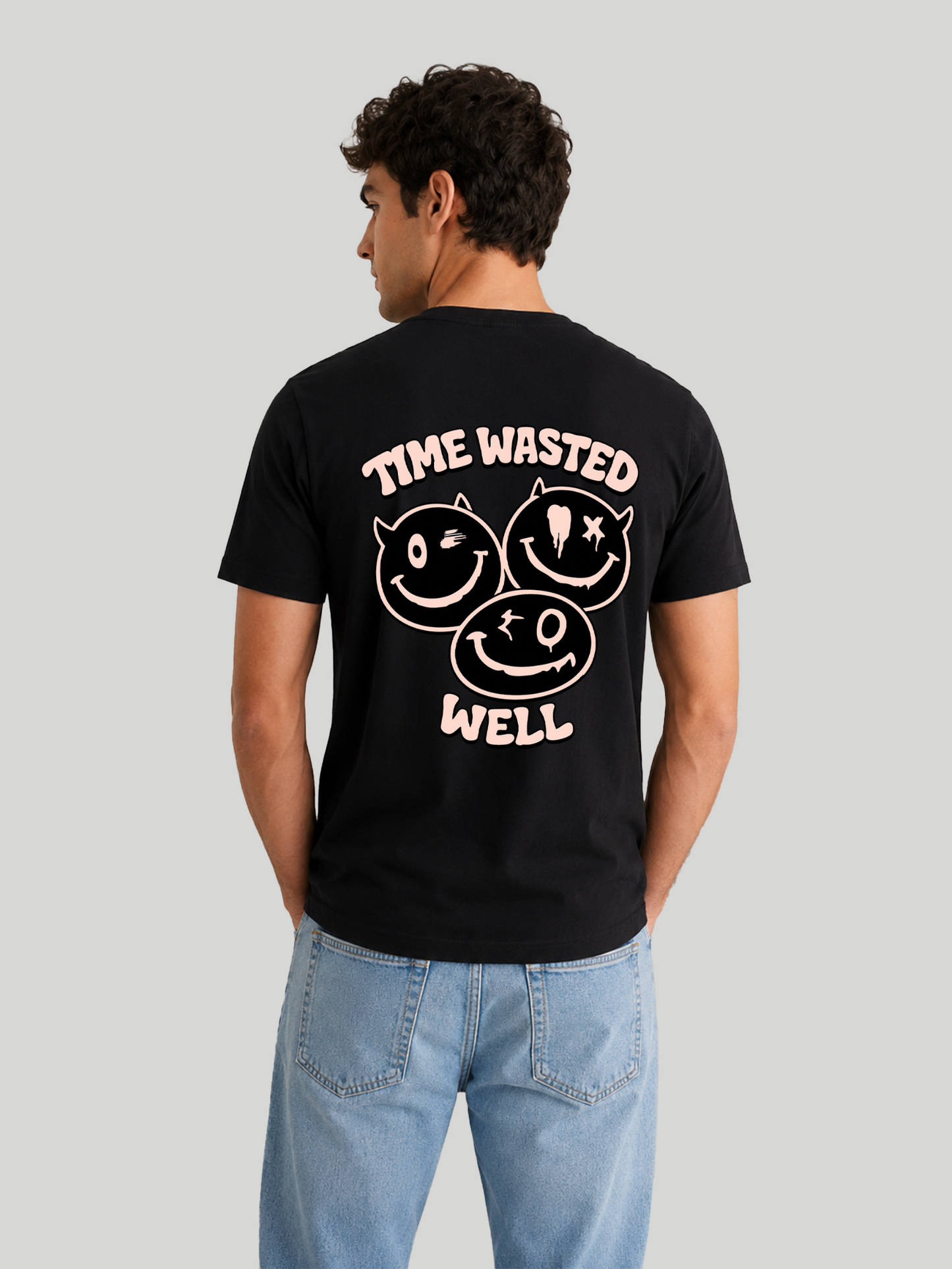 The back view of a male model looking slightly over his shoulder, wearing a black cotton half-sleeve t-shirt with a light pink graphic print reading "TIME WASTED WELL" alongside three edgy cartoon smileys.
