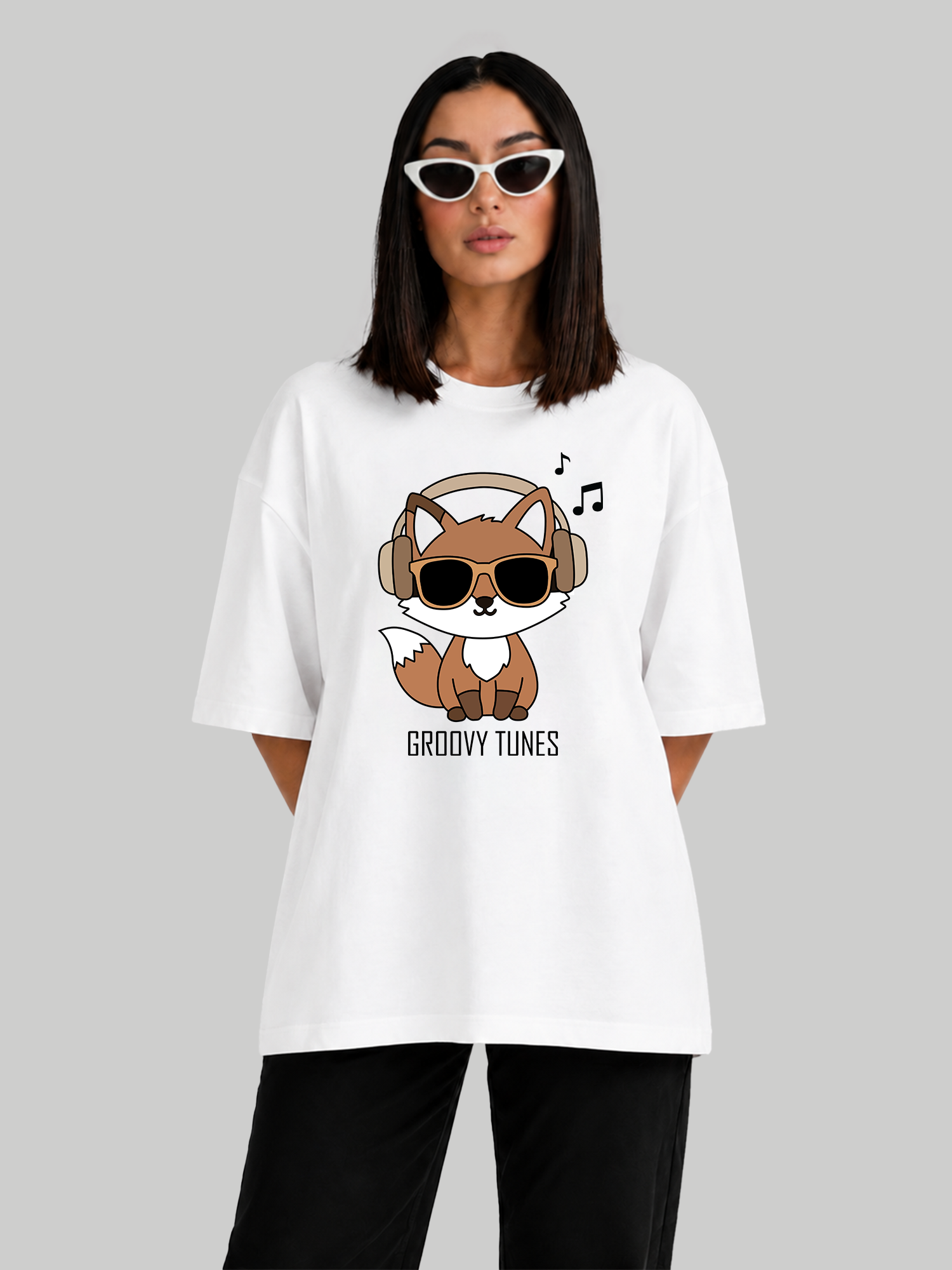 Women's oversized white t-shirt featuring a Groovy Tunes fox graphic with headphones and sunglasses, front view with hands behind back.
