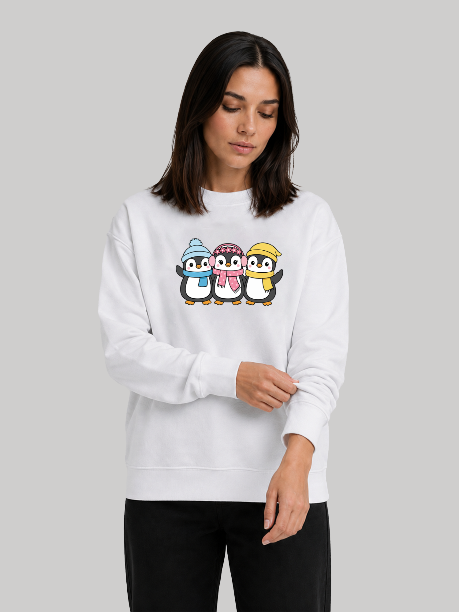 A female model looking down slightly while rolling up the sleeve of a white graphic sweatshirt featuring a cute penguin illustration.