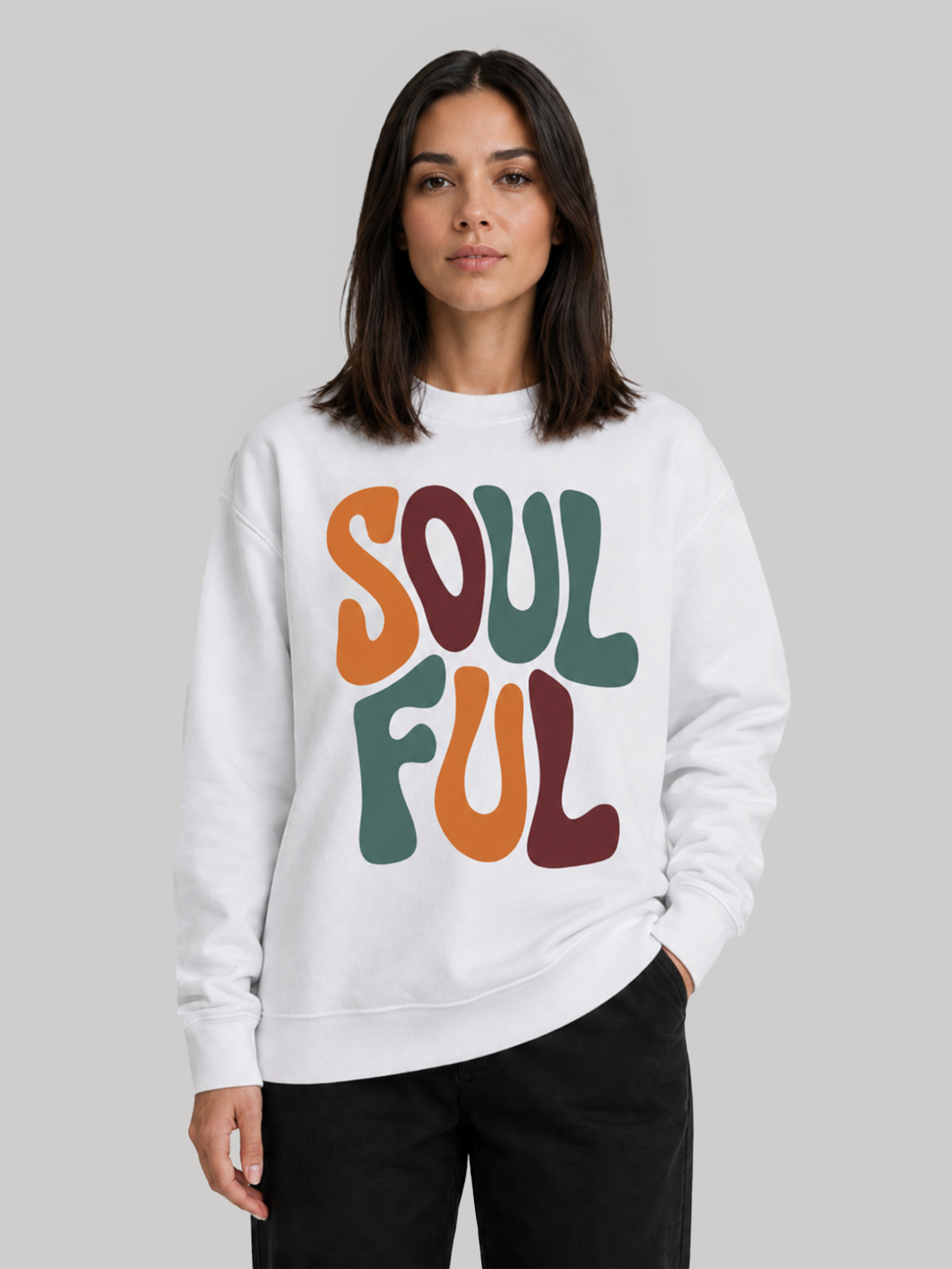 A front view of a female model standing with one hand in her pocket, showcasing a relaxed-fit white sweatshirt with a multi-colored font pattern.