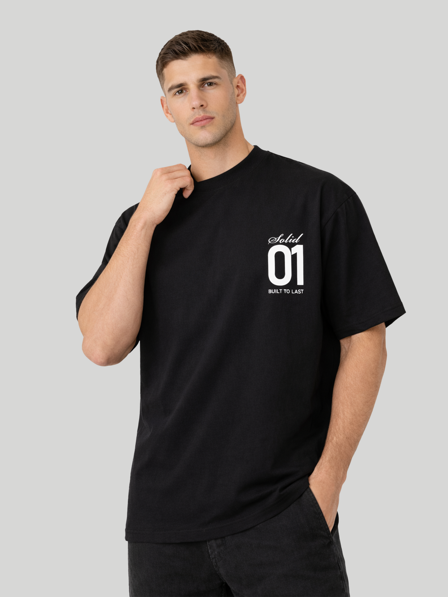 Man wearing black oversized t-shirt with Solid 01 chest print in angled pose with hand near neck