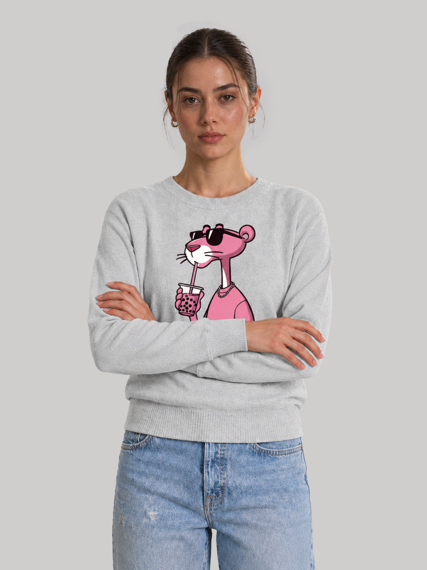 A front studio shot of a female model standing with her arms crossed, wearing a casual melange grey sweatshirt with a pink cartoon character print.