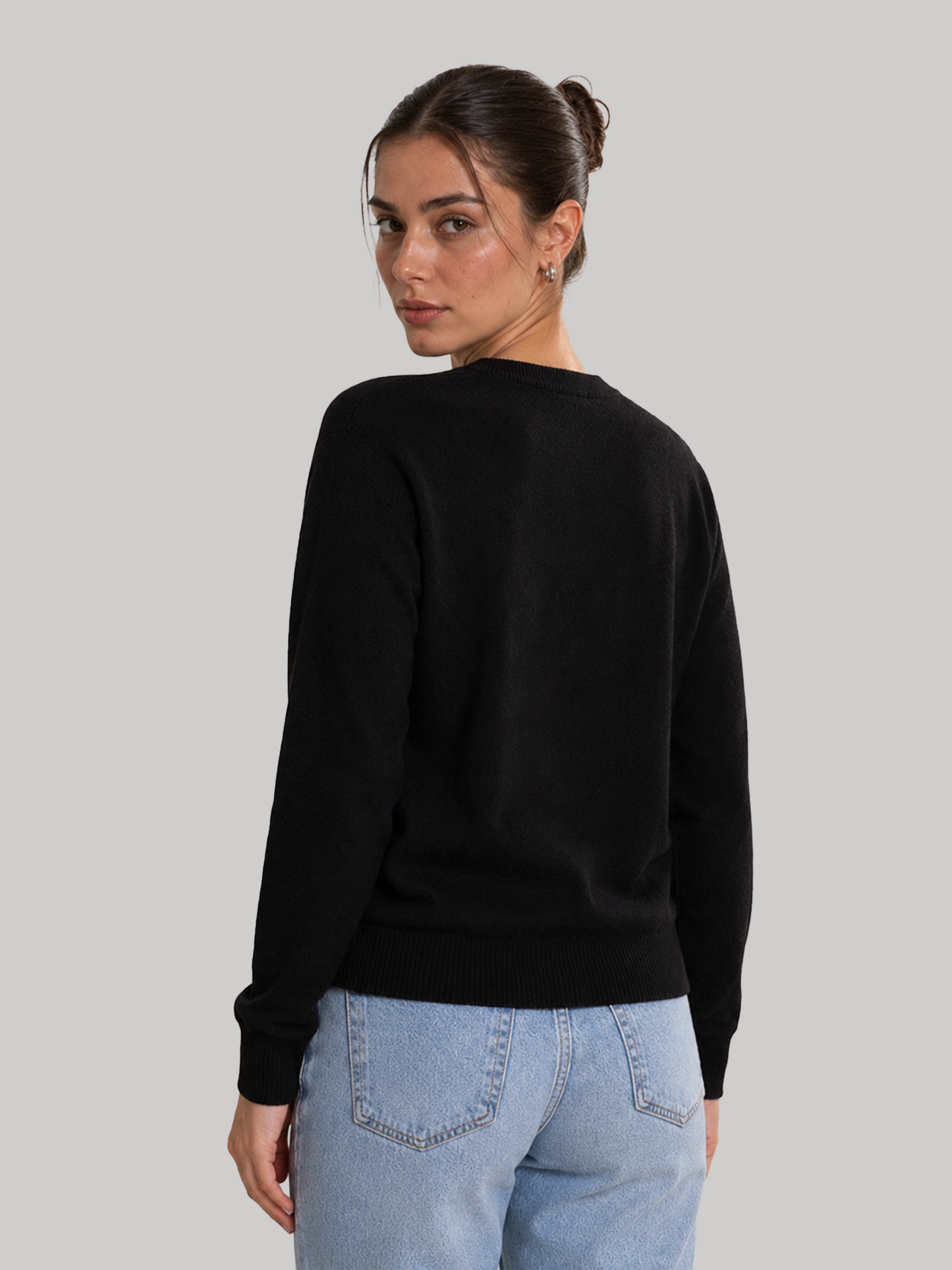 A rear view over the shoulder of a female model wearing a solid black sweatshirt, showcasing the back fit and clean fabric structure.