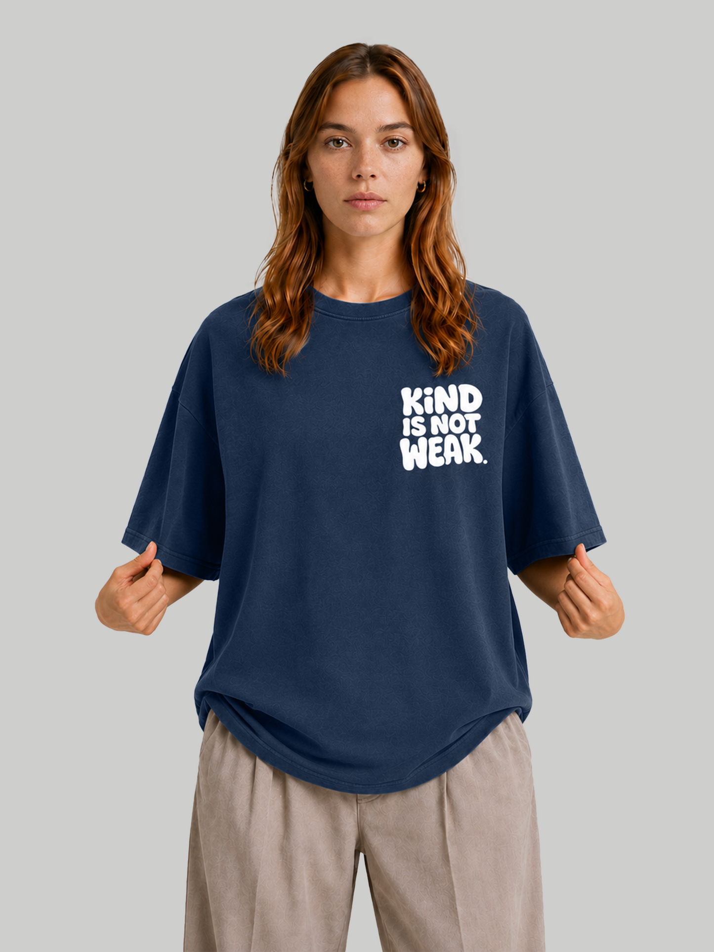 Women's oversized navy blue t-shirt with "Kind Is Not Weak" chest graphic, model holding hem.