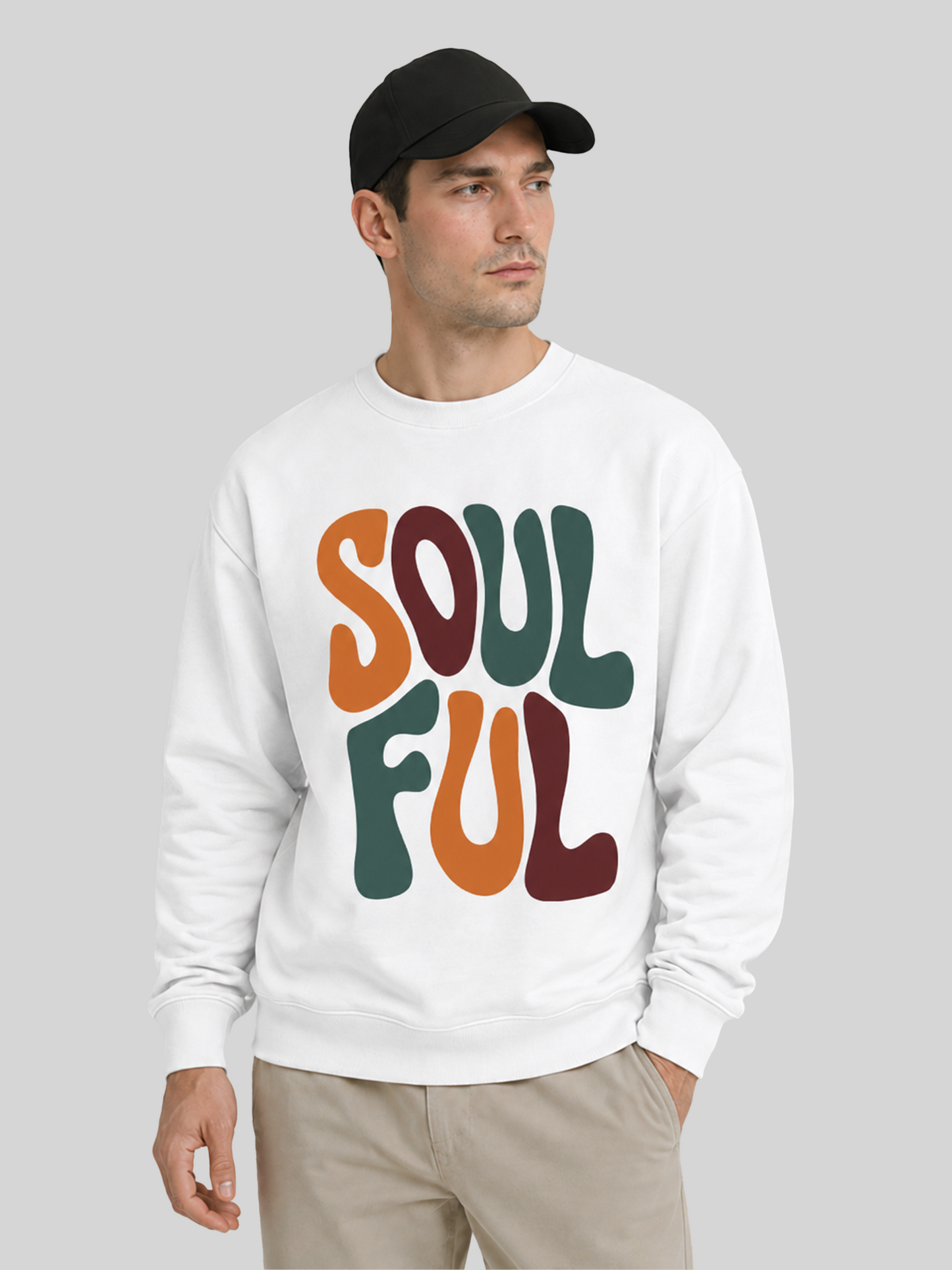 A close-up portrait shot of a male model in a black cap and a white graphic sweatshirt featuring a multi-colored retro text print.