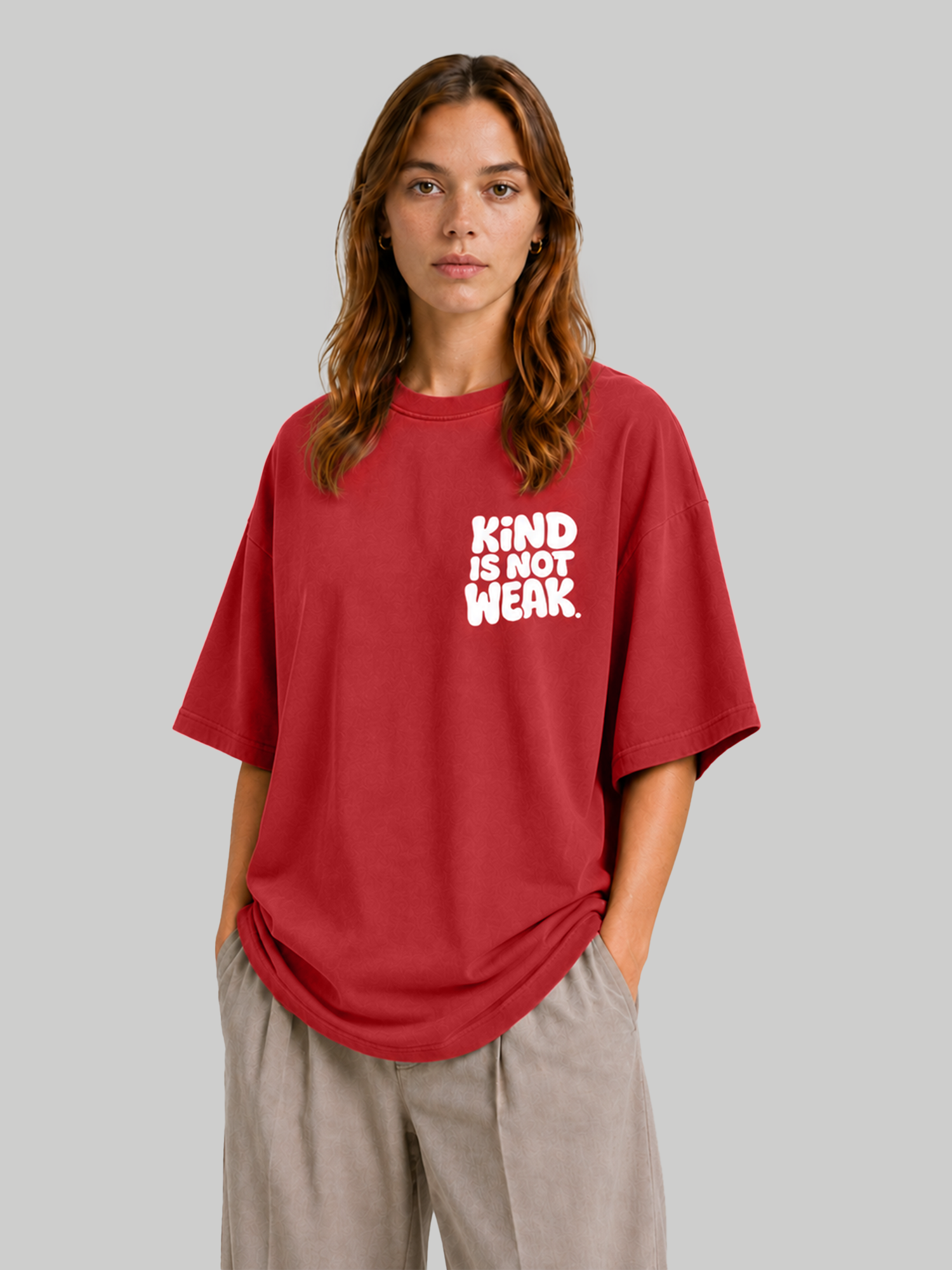 Women's oversized red graphic t-shirt with "Kind Is Not Weak" print, angled front view with hands in pockets.