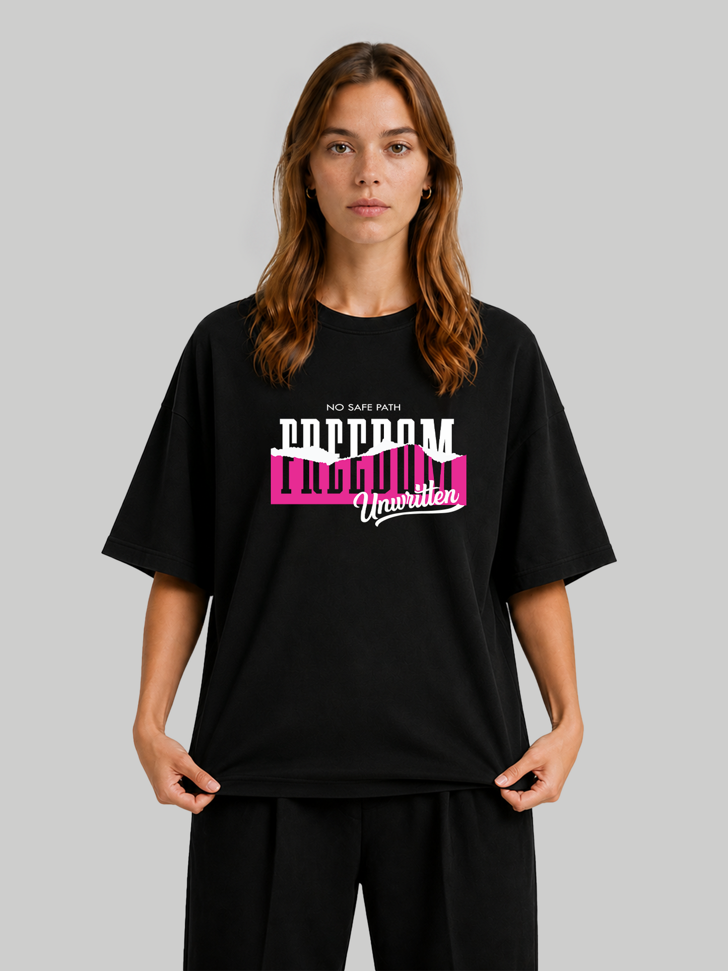 Women's oversized black graphic tee featuring bold "Freedom Unwritten" text design, front view holding the hem.