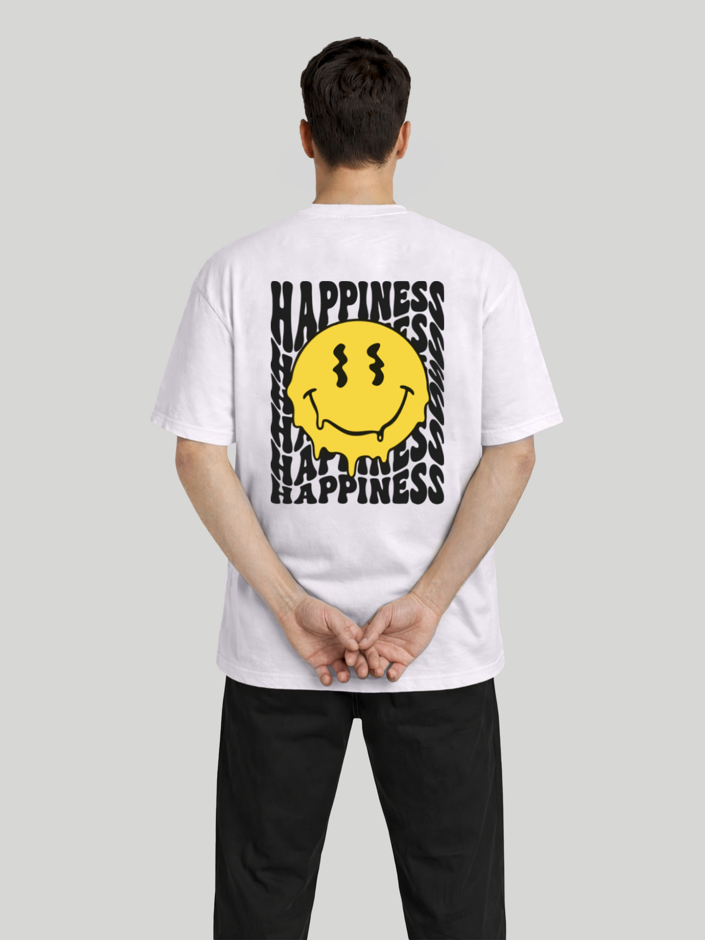 Back view of man wearing orchid oversized t-shirt with Happiness back graphic and yellow dripping smiley print with hands clasped behind