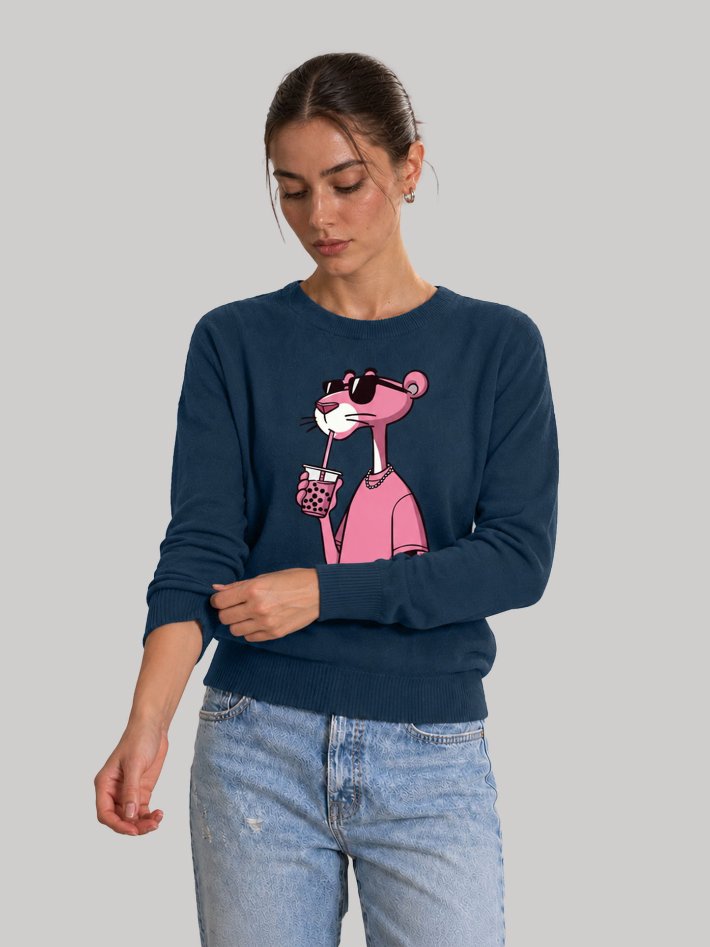 A female model looking down while rolling up the sleeve of a navy blue long-sleeve sweatshirt featuring a graphic print of a pink character wearing sunglasses.