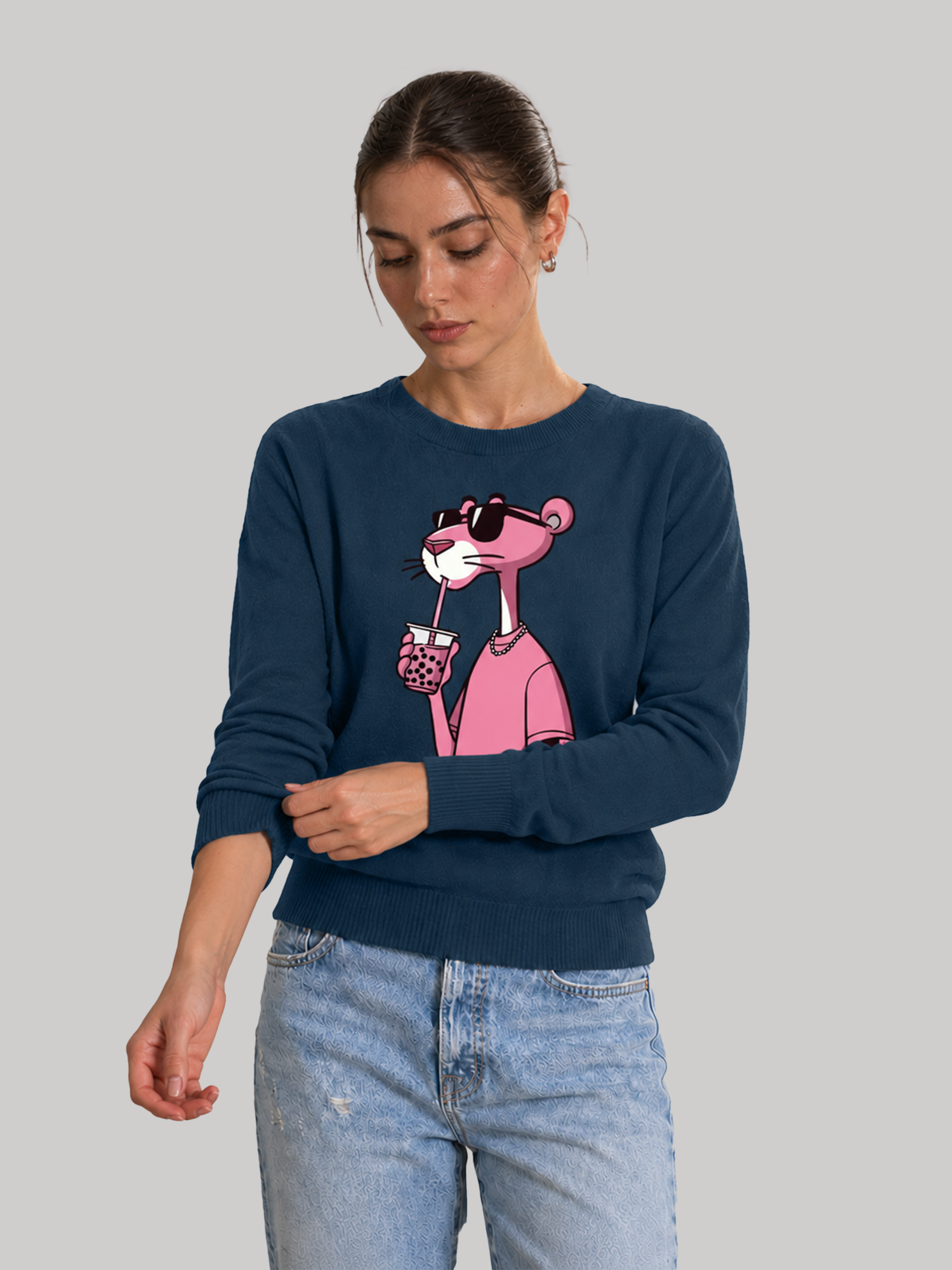 A female model looking down while rolling up the sleeve of a navy blue long-sleeve sweatshirt featuring a graphic print of a pink character wearing sunglasses.