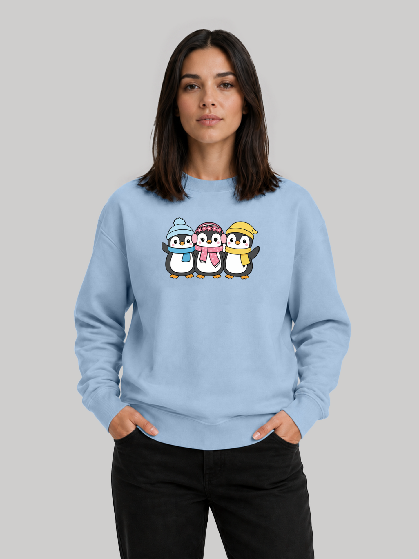 A front studio shot of a female model posing with hands in her pockets, wearing a casual baby blue sweatshirt with a winter-themed print.