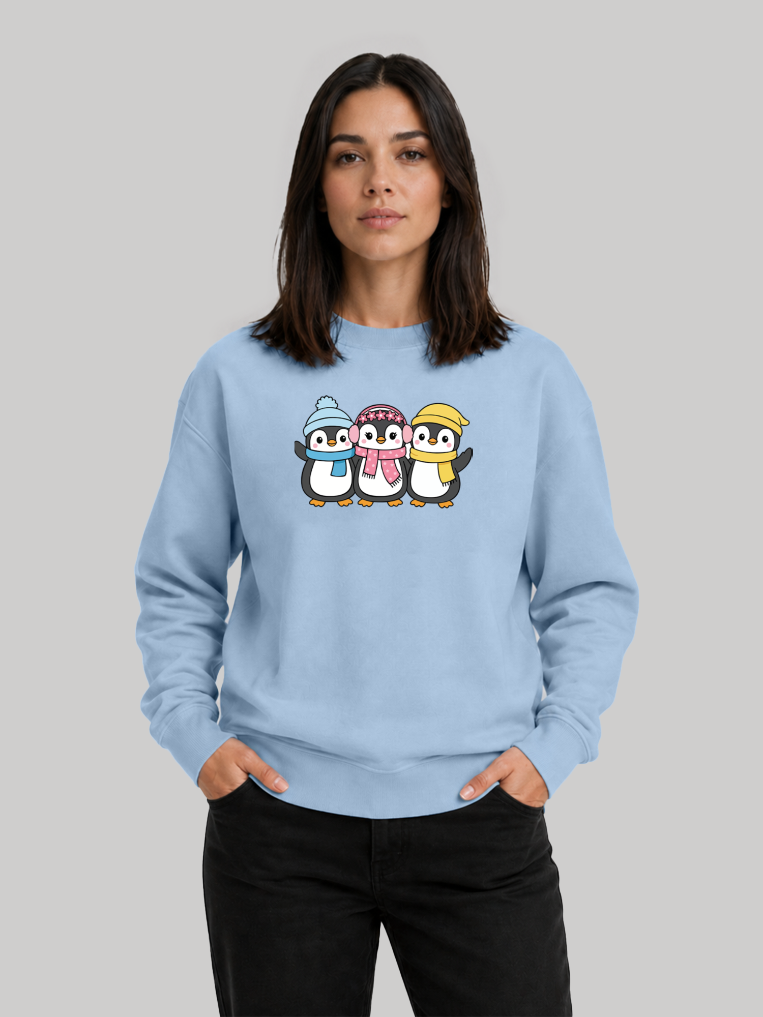 A front studio shot of a female model posing with hands in her pockets, wearing a casual baby blue sweatshirt with a winter-themed print.