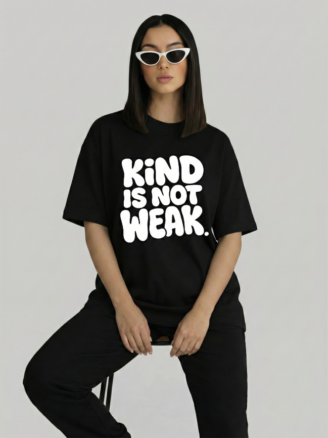 Women’s black oversized graphic t-shirt with Kind Is Not Weak print sitting pose