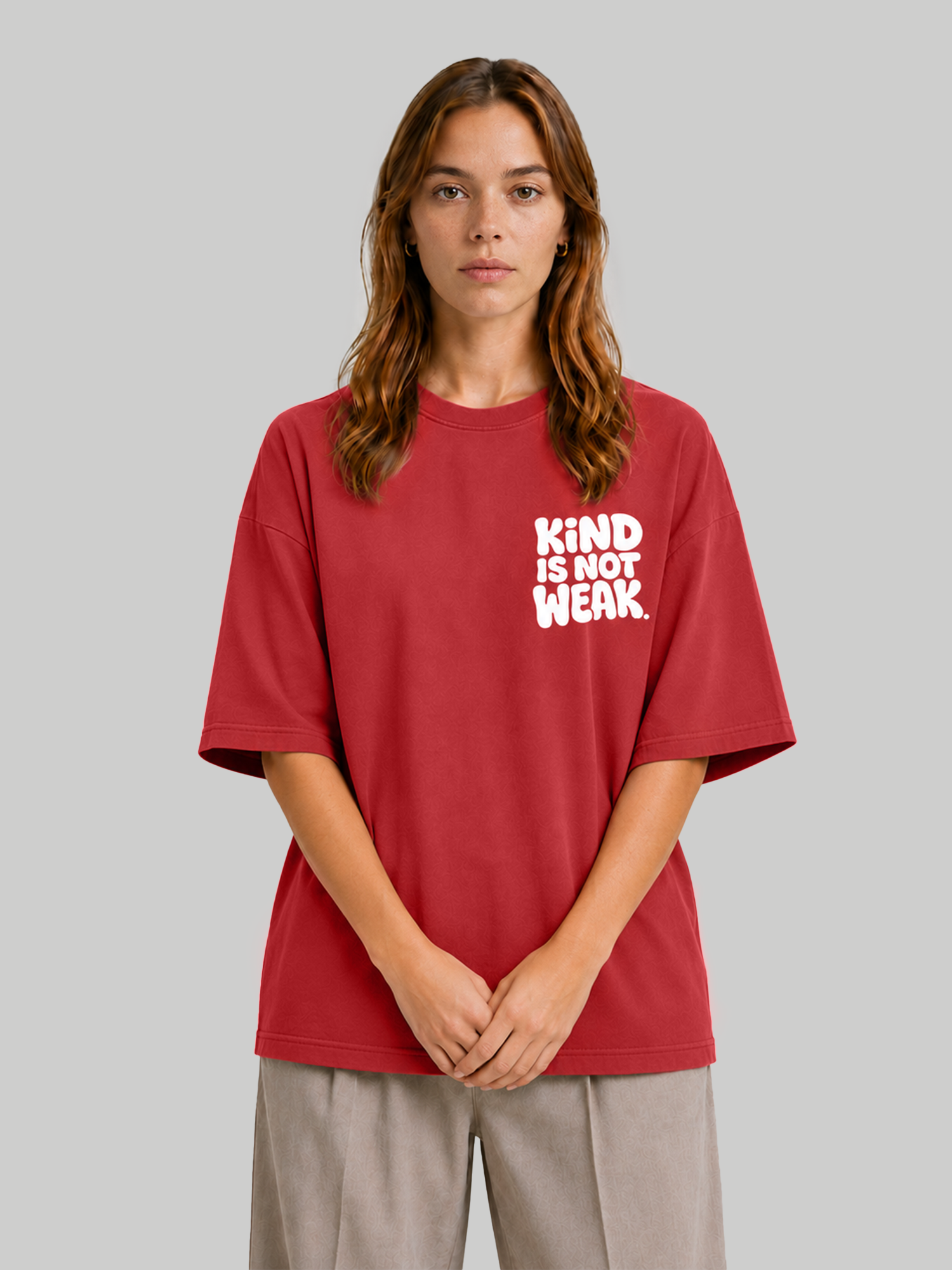 Women's oversized red t-shirt with "Kind Is Not Weak" chest graphic, model standing with hands clasped.