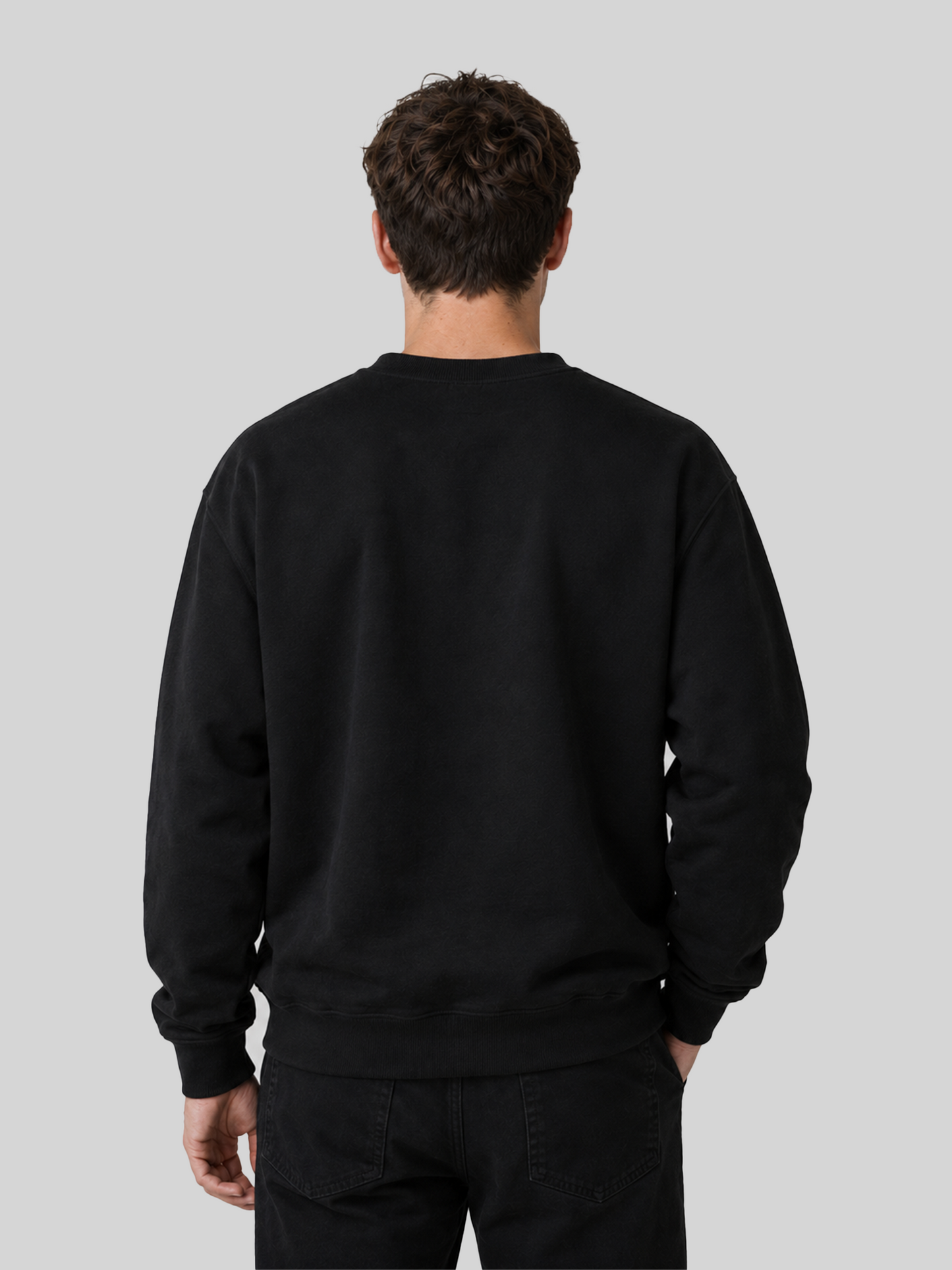 The back view of a male model wearing a solid black long-sleeve sweatshirt and black jeans, showcasing a clean, minimalist fit.