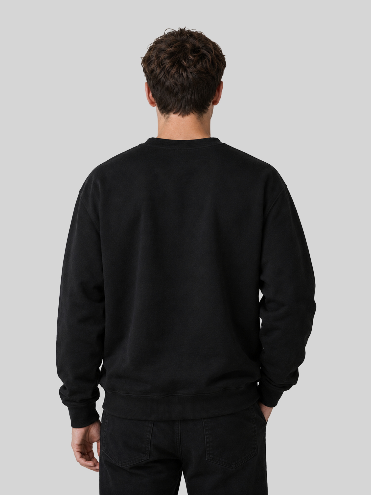 The back view of a male model wearing a solid black long-sleeve sweatshirt and black jeans, showcasing a clean, minimalist fit.